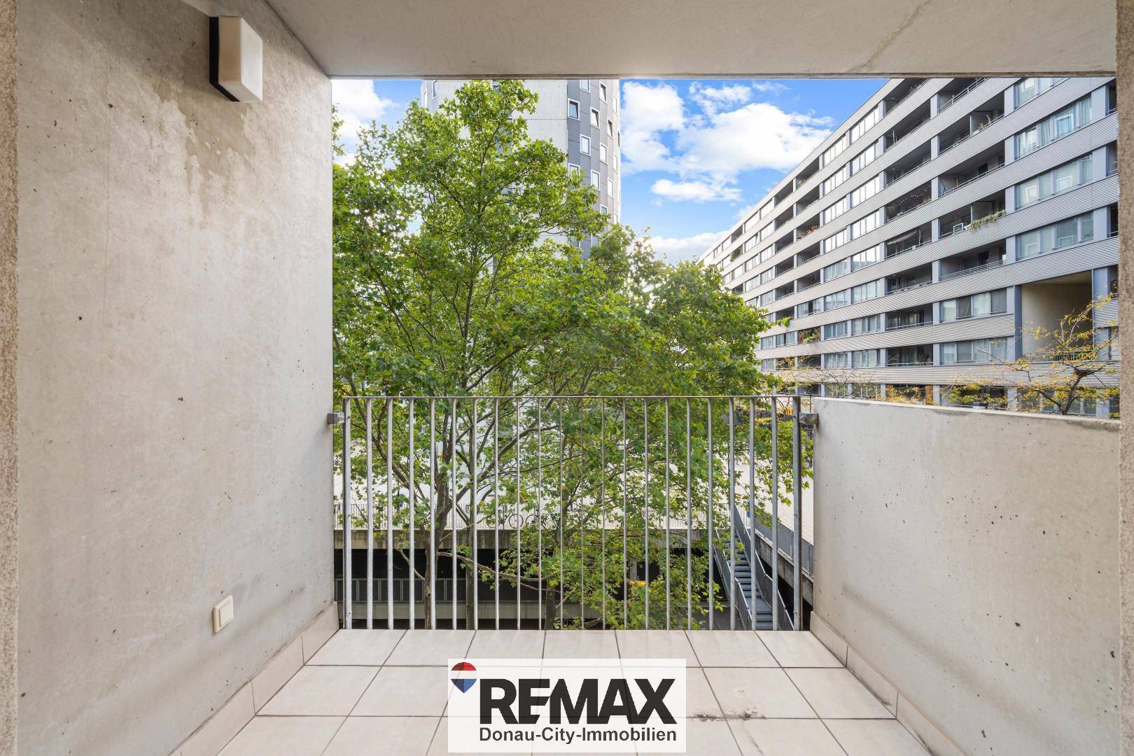 Balkon mit Fliesenboden und freiem Blick auf grüne Bäume und moderne Gebäude.