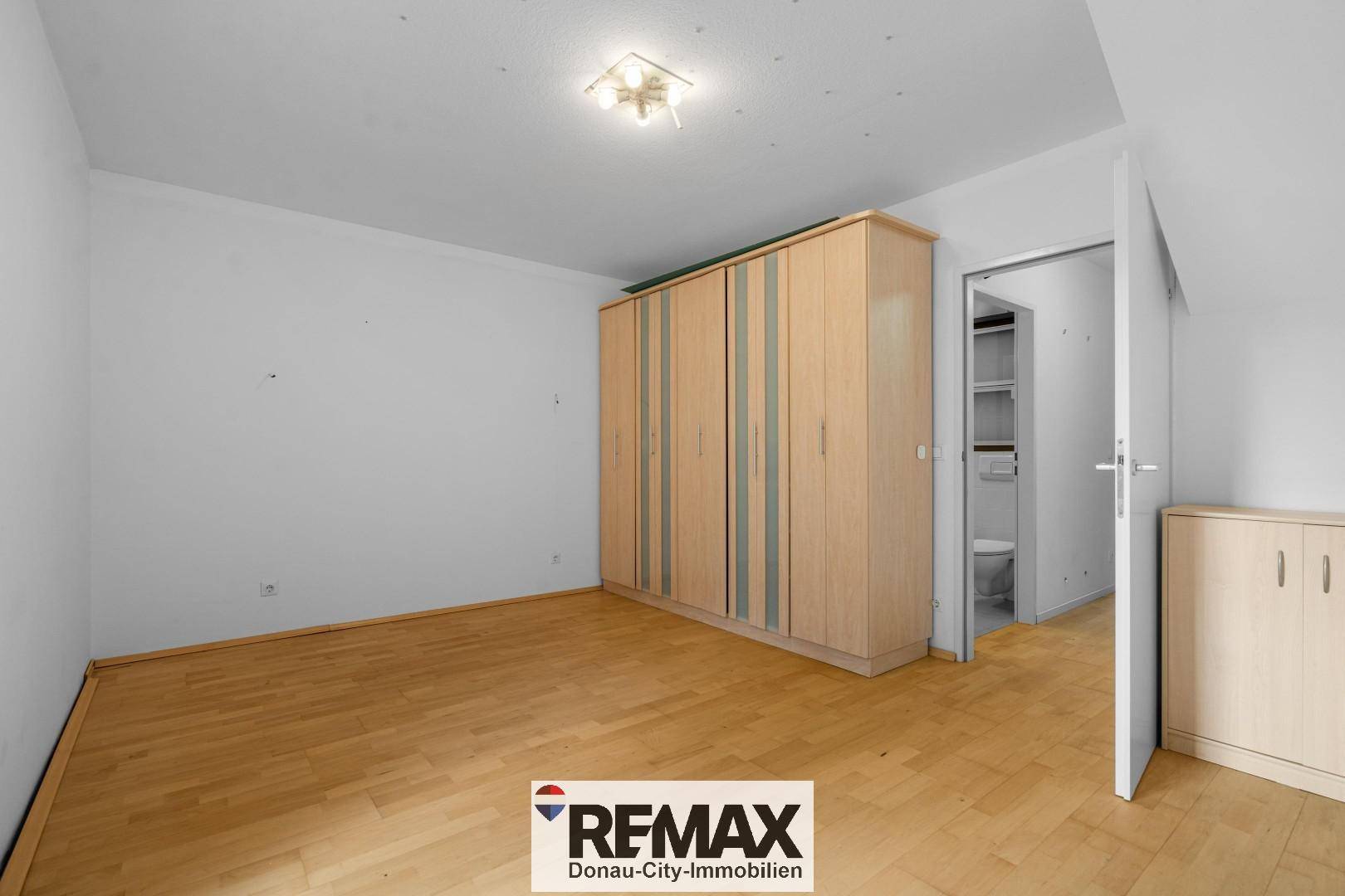 Schlafzimmer mit Holzboden, großem Kleiderschrank und Zugang zu einem angrenzenden Bad.