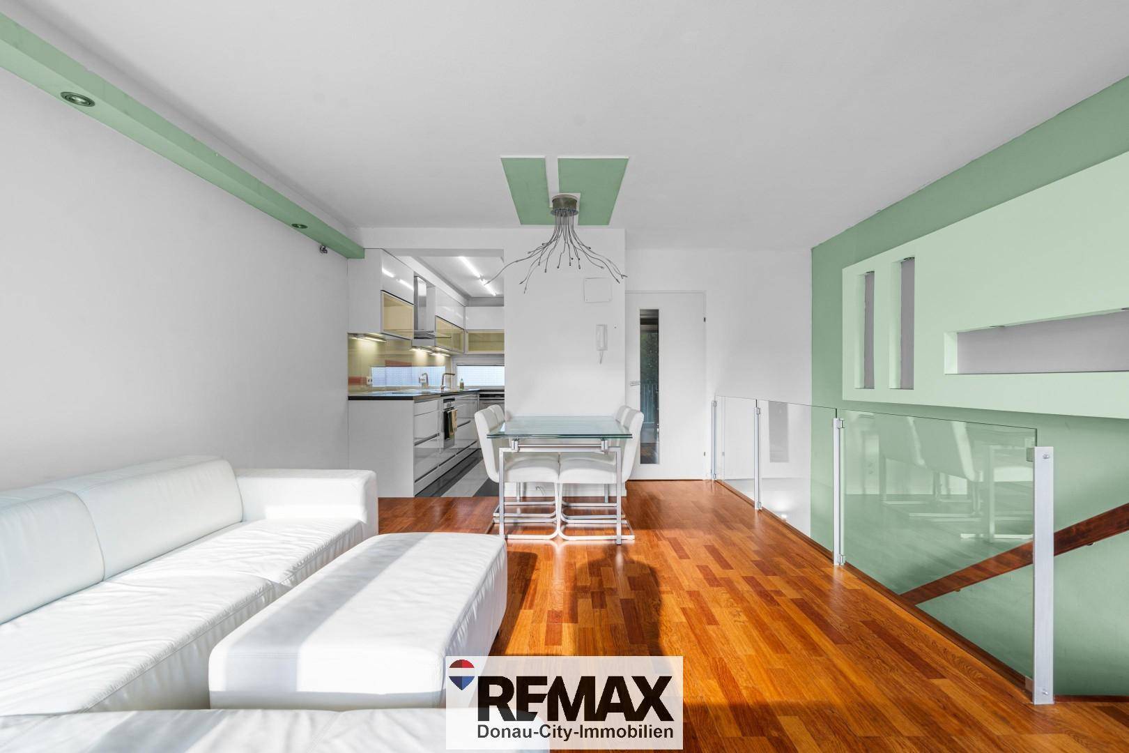 Offener Wohn-Essbereich mit Holzboden, weißem Sofa und moderner Küche im Hintergrund.