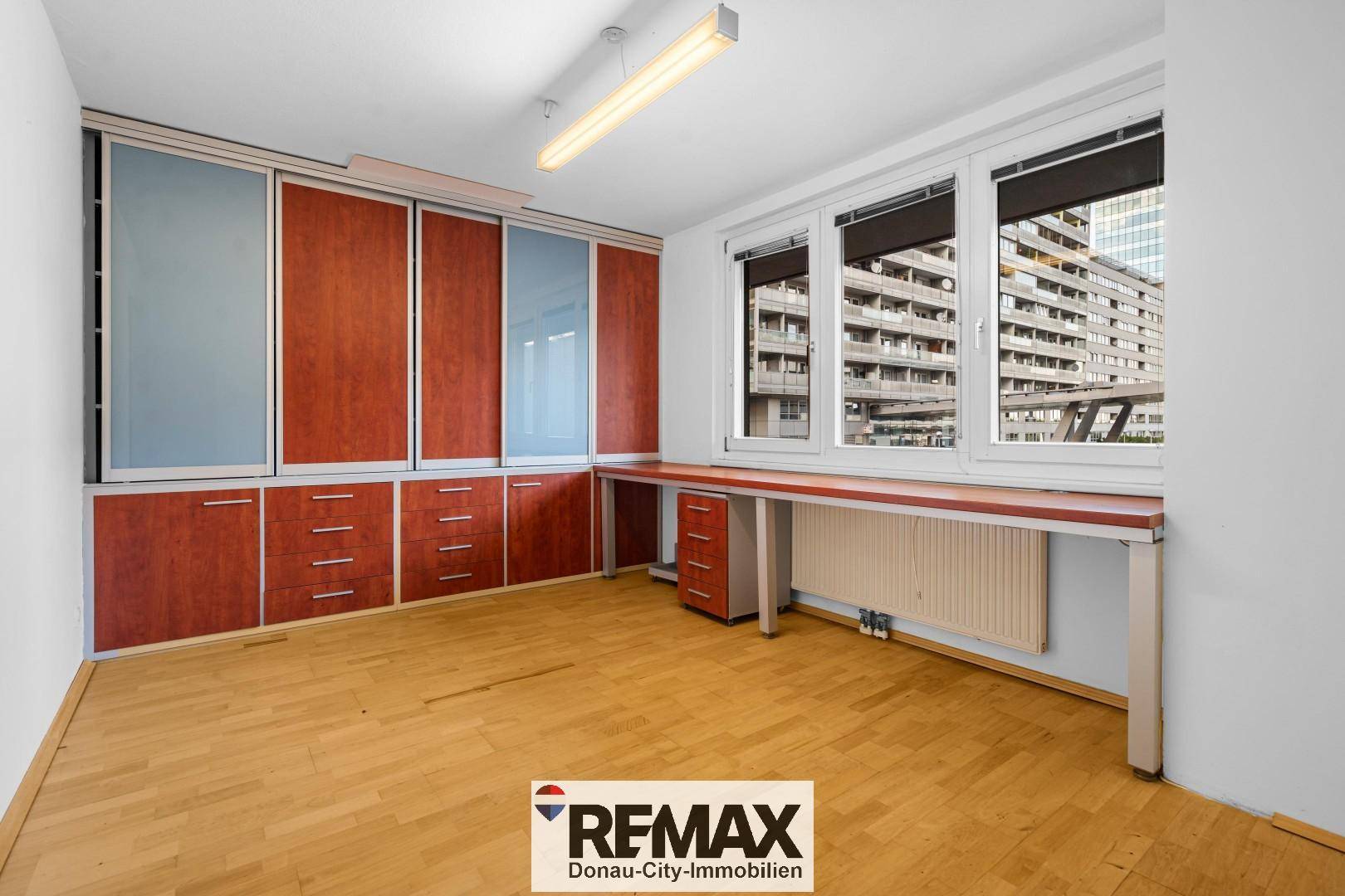 Helles Arbeitszimmer mit Holzboden, Einbauschränken und großzügiger Fensterfront.