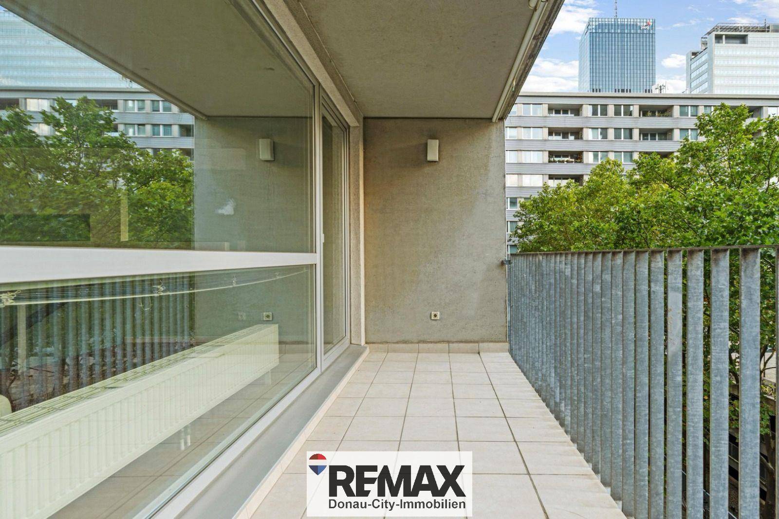 Geräumiger Balkon mit Fliesenboden und Blick auf die umliegenden Gebäude und Bäume.