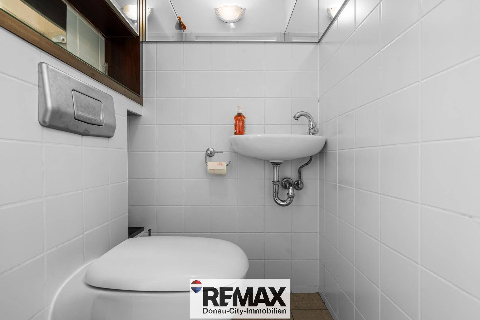 Separates WC mit Wandfliesen, kleinem Waschbecken und wandhängender Toilette.