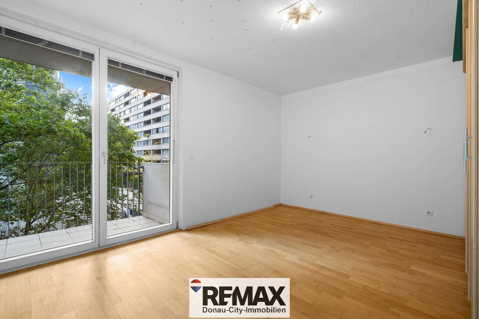 Leeres Schlafzimmer mit Holzboden und großem Fenster mit Zugang zum Balkon.