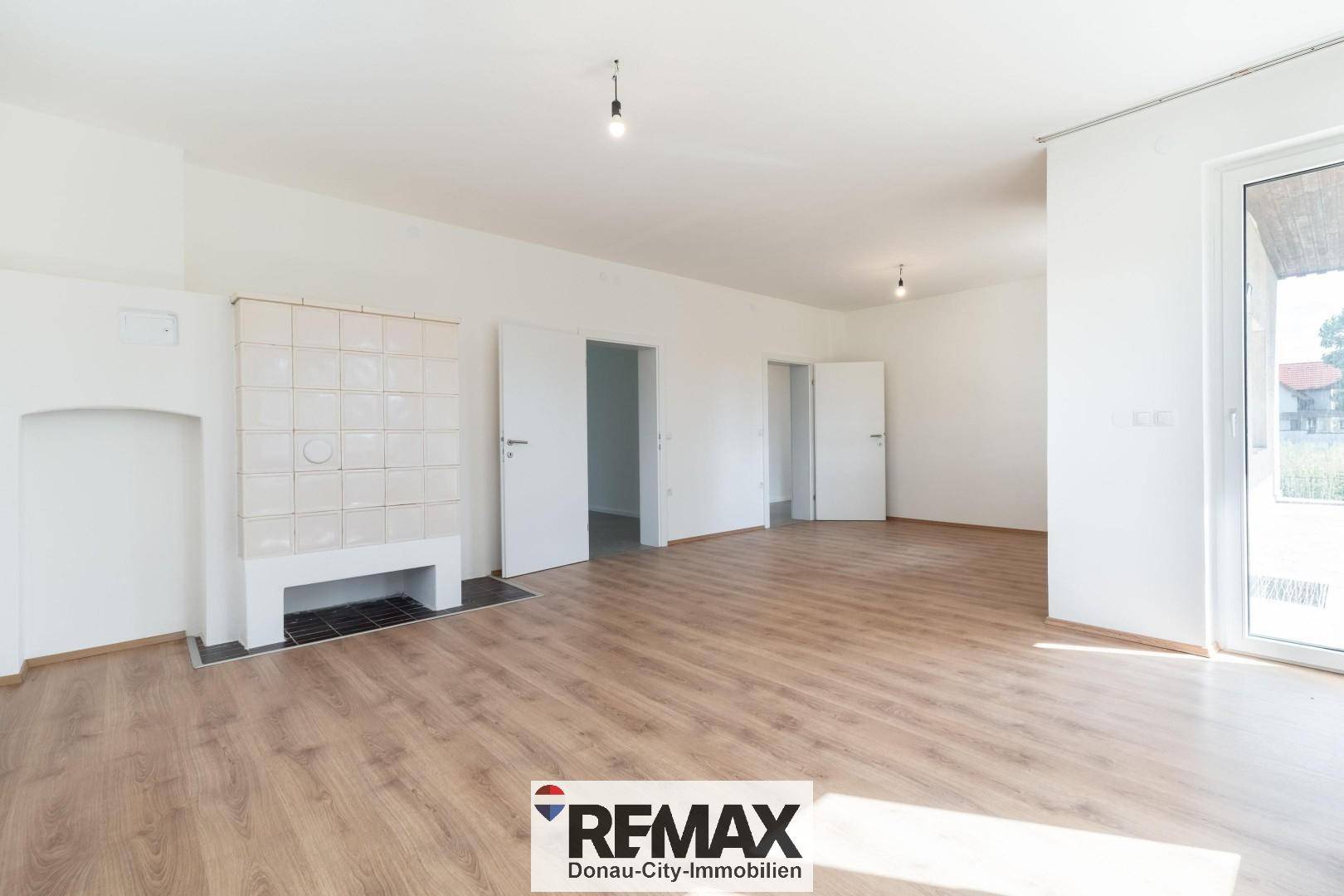 Großes Wohnzimmer mit Laminatboden, Kachelofen und Zugang zur Terrasse.