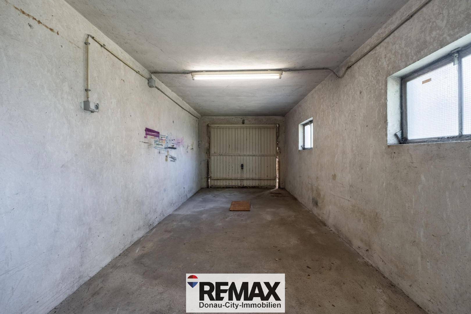 Geräumige Garage mit Betonboden, Rolltor und kleinen Fenstern.