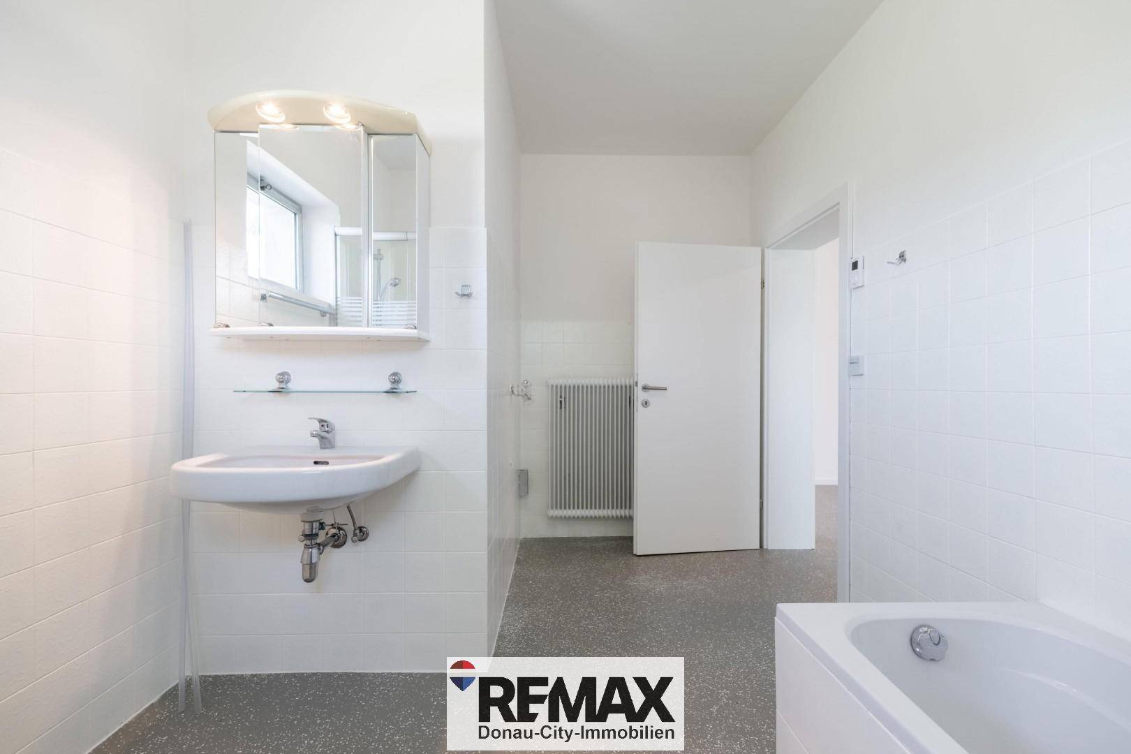 Badezimmer mit Badewanne, Waschbecken, Spiegelschrank und weiß gefliesten Wänden.