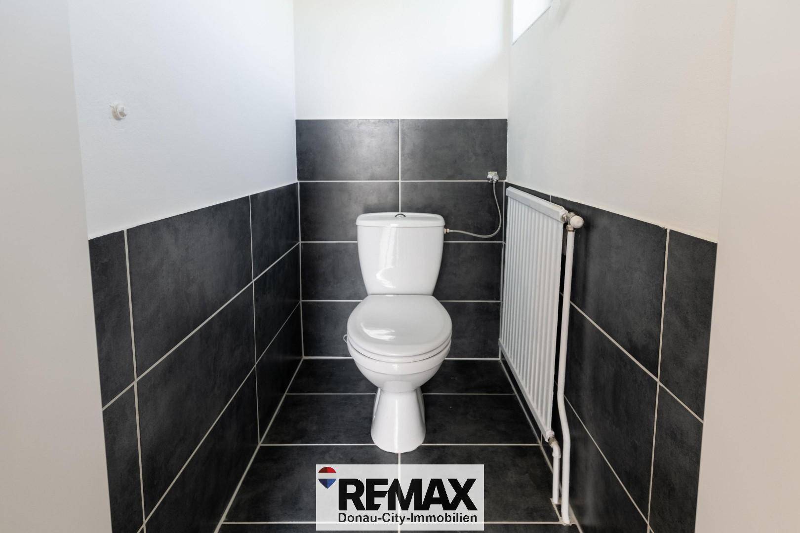 Separate Toilette mit dunklen Fliesen und Heizkörper.