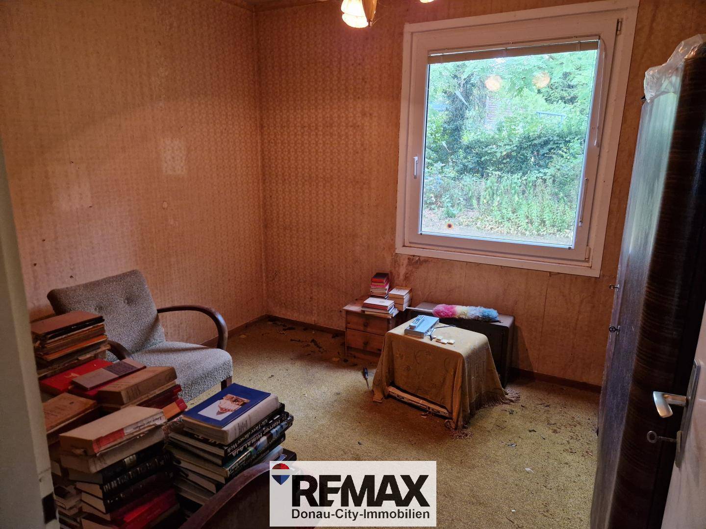 Schlafzimmer oder Arbeitszimmer mit Teppichboden, vielen Büchern und Fensterblick ins Grüne.