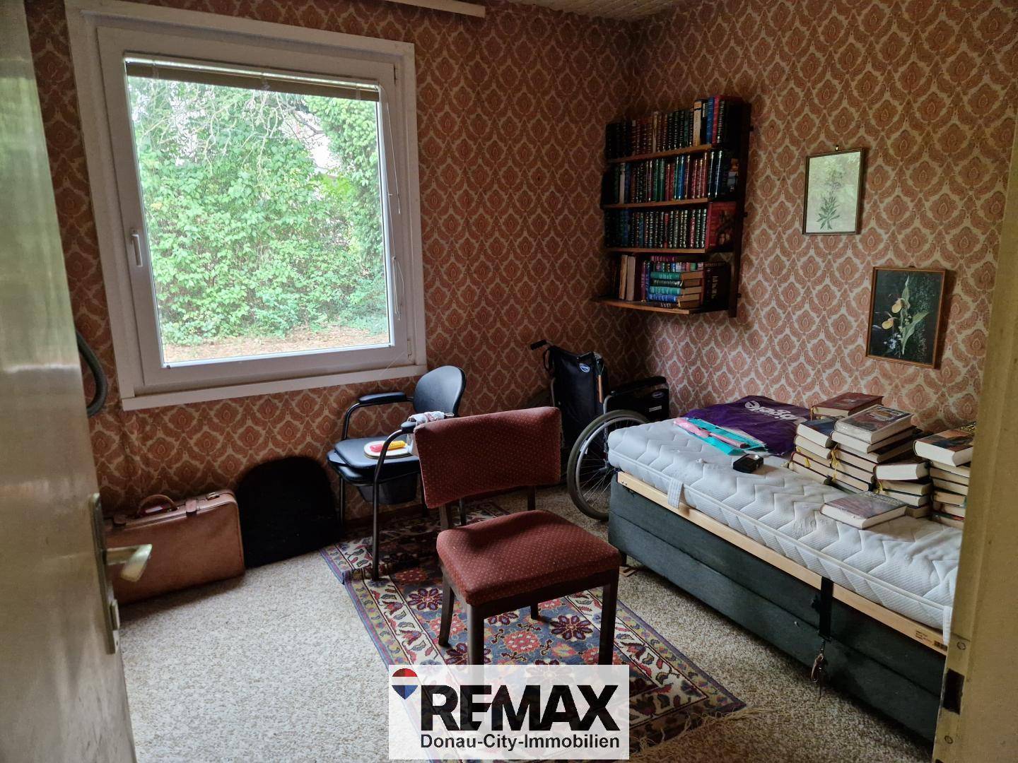 Schlafzimmer mit Einzelbett, Teppichboden, gemusterter Tapete und Bücherregal.