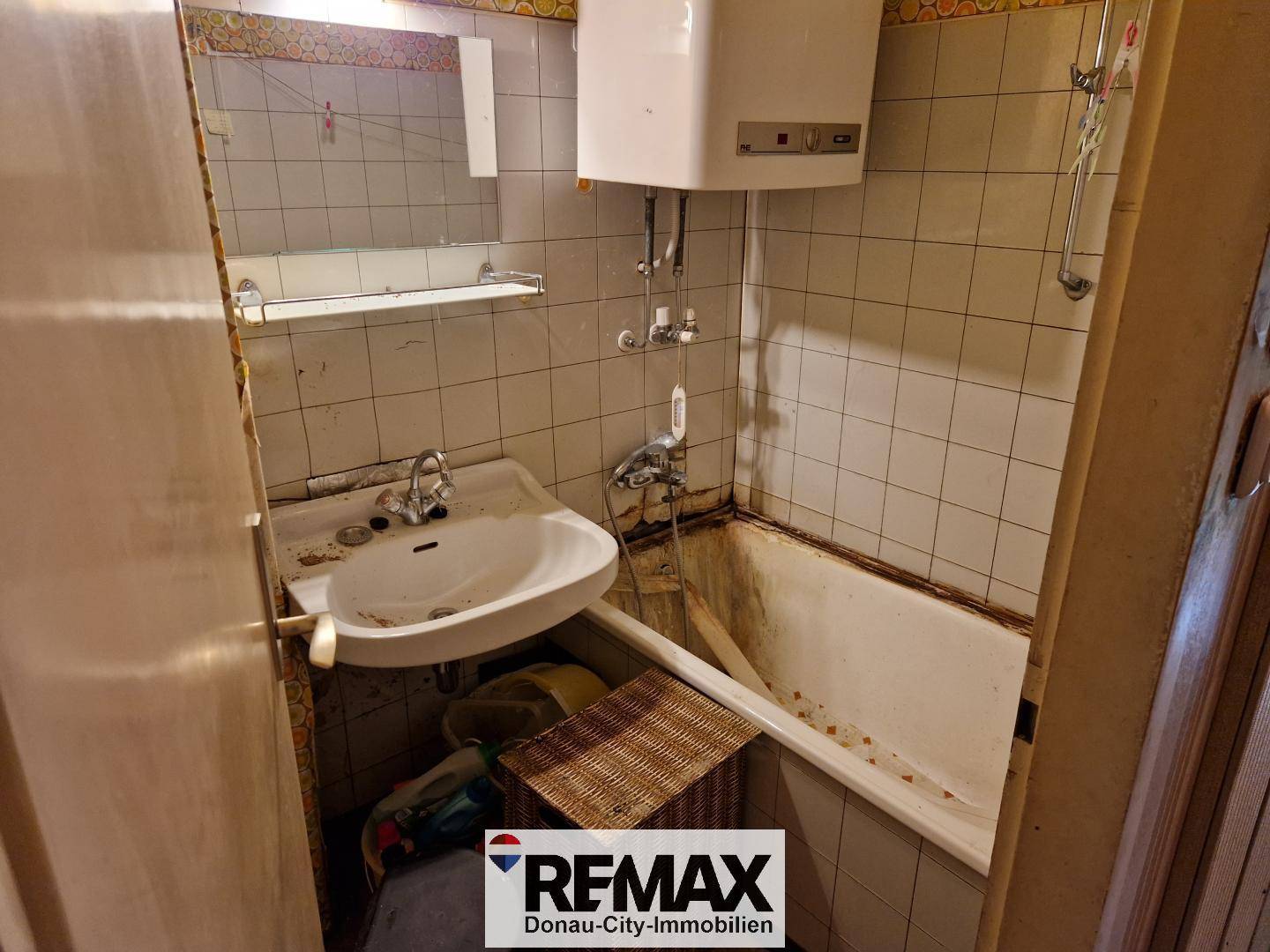Älteres Badezimmer mit Badewanne, Waschbecken und Wandfliesen, das Renovierung benötigt.