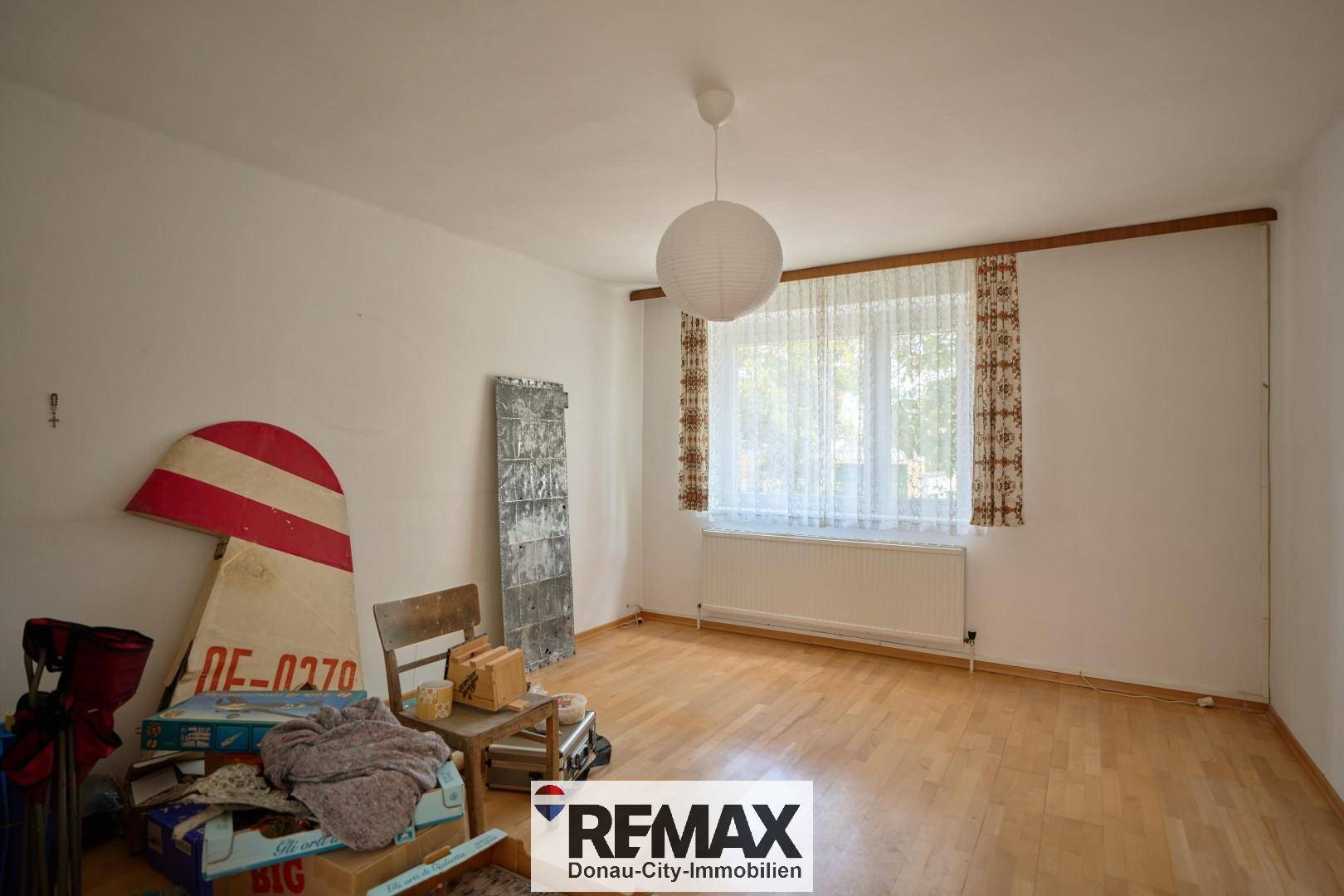 Helles Zimmer mit Holzboden, großem Fenster und verschiedenen Gegenständen.