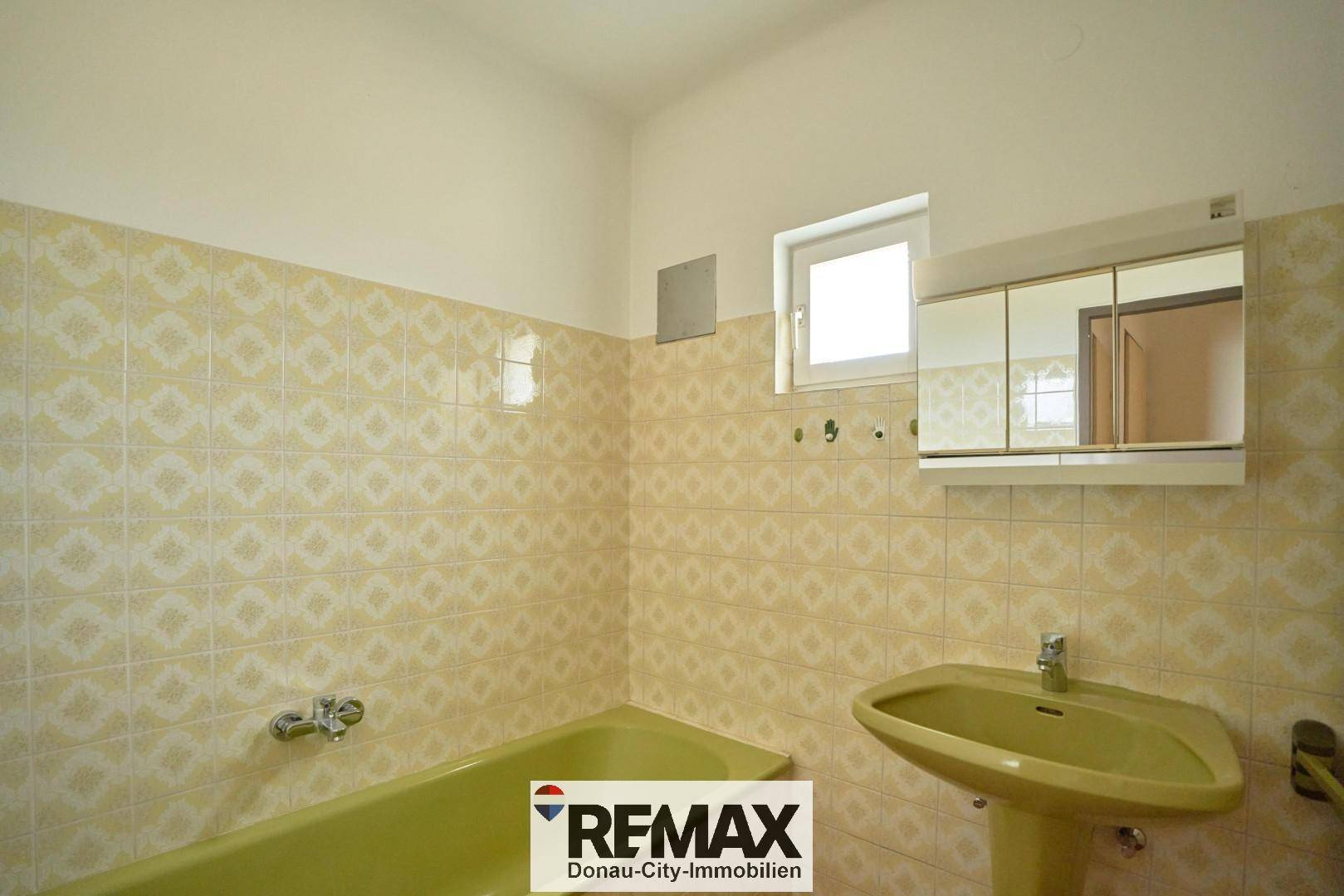 Badezimmer mit gelben Fliesen, passender Badewanne und Waschbecken, sowie einem kleinen Fenster.