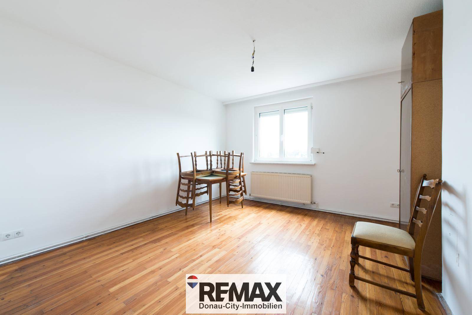 Geräumiges Zimmer mit Holzparkettboden und einem kleinen Esstisch mit Stühlen.