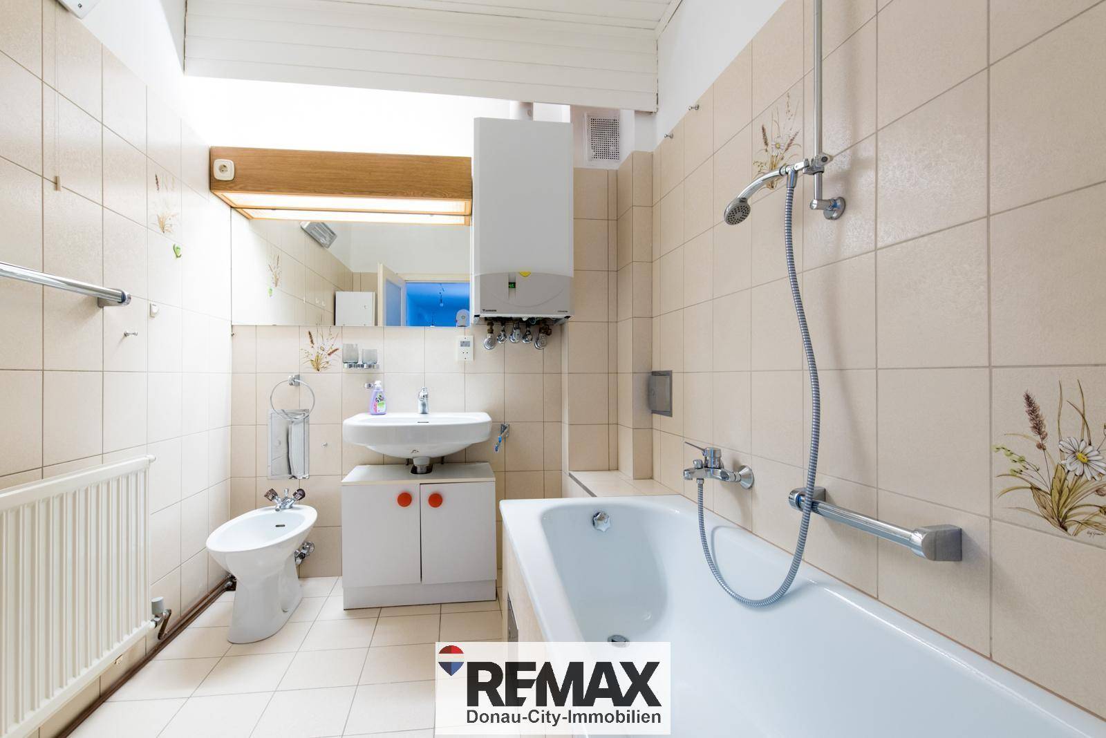 Badezimmer mit beigefarbenen Fliesen, Badewanne, Waschbecken und Bidet.