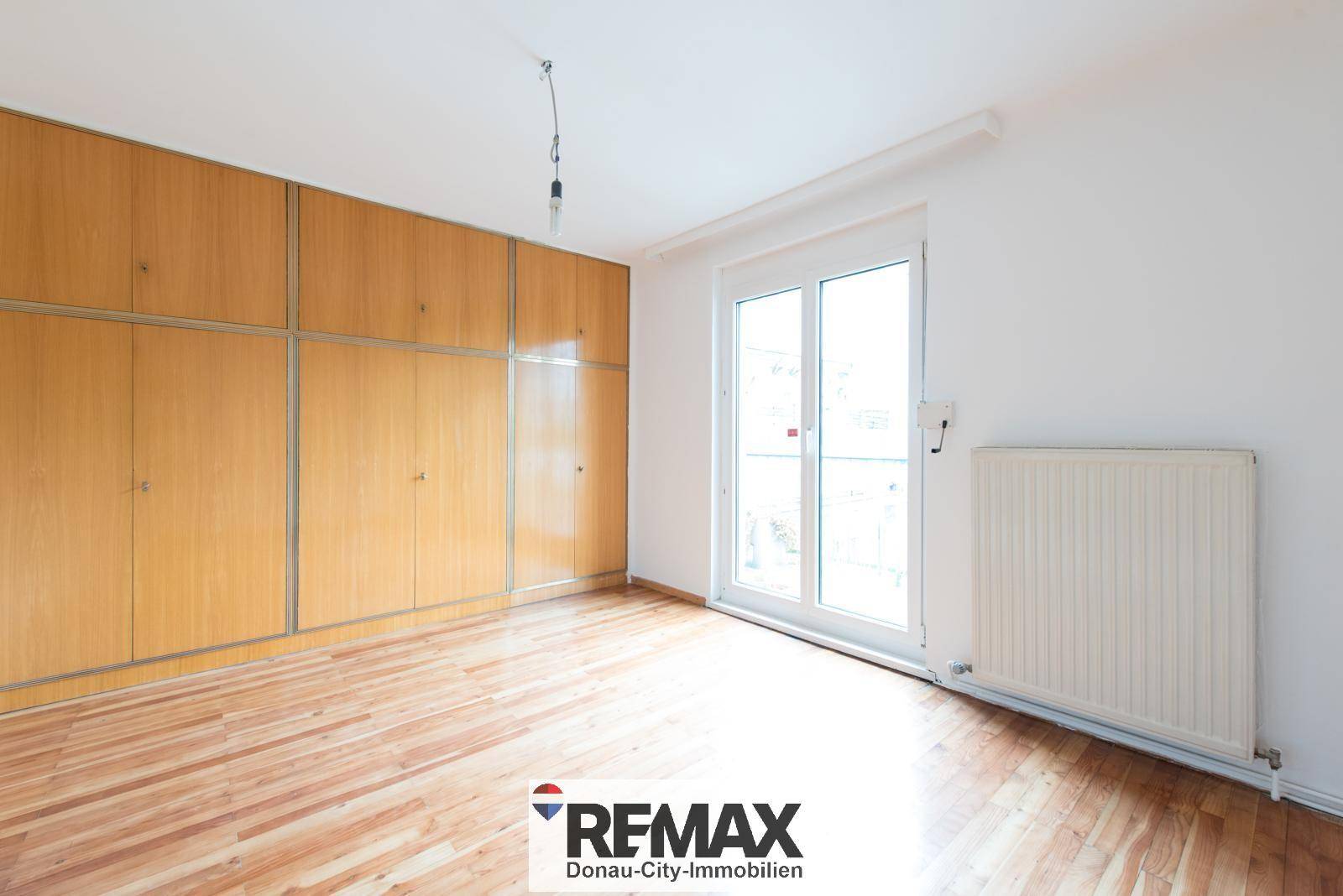 Geräumiges Zimmer mit Holzboden, großen Einbauschränken und Zugang zum Außenbereich.