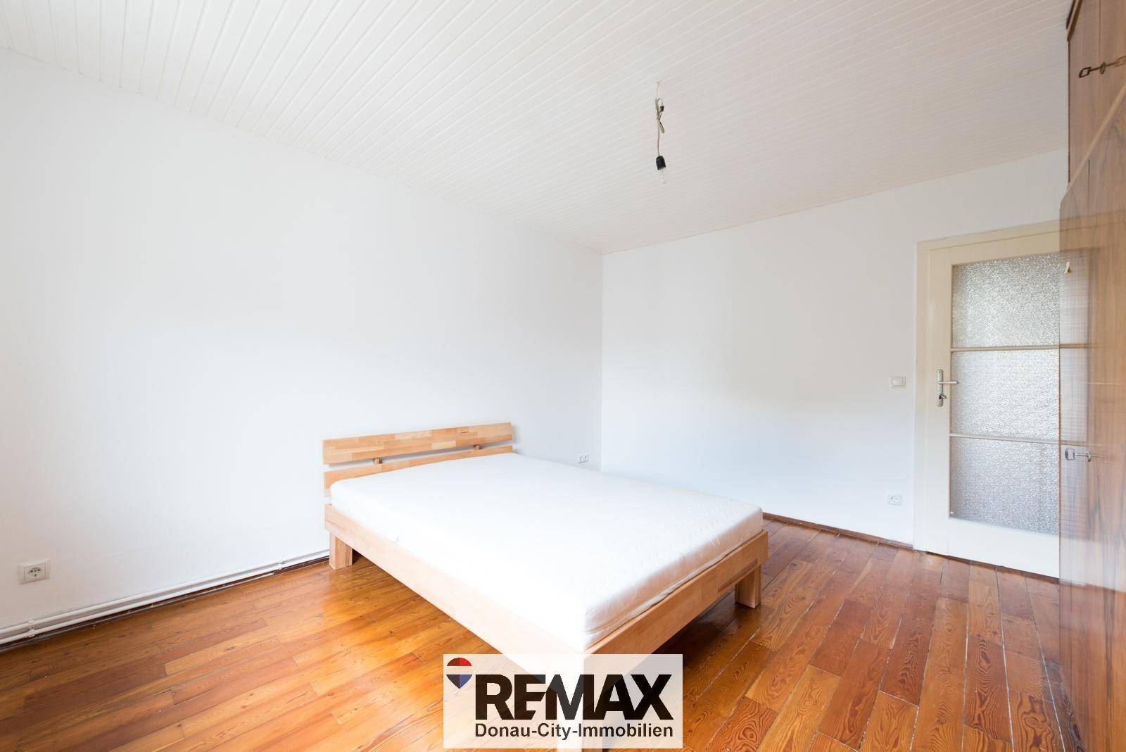 Helles Schlafzimmer mit Holzboden und einem einfachen Holzrahmenbett.