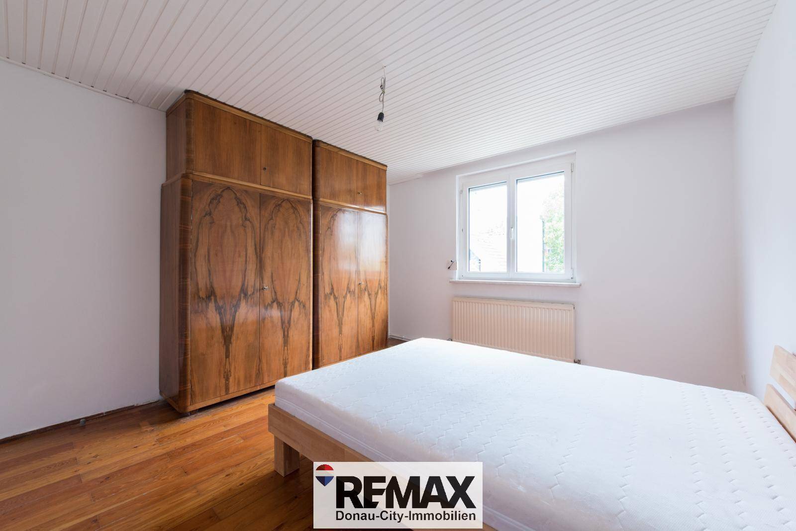 Schlafzimmer mit Holzboden, einem Bett und einem großen Holzschrank.