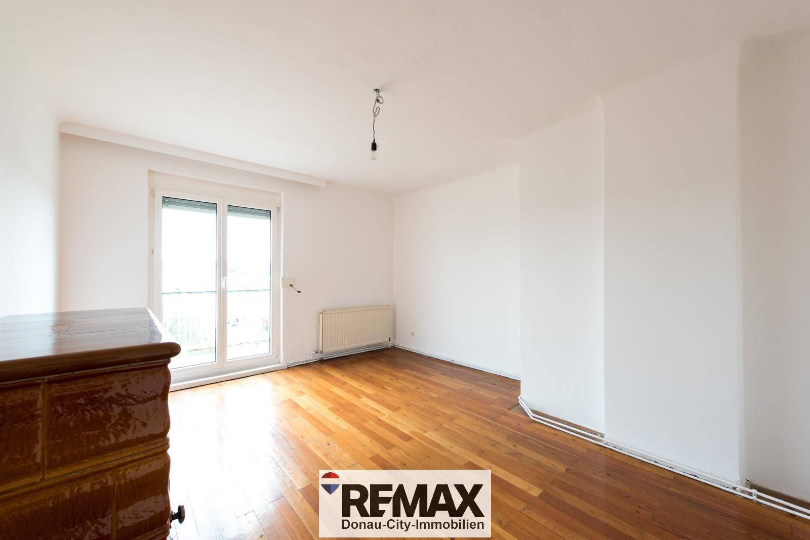 Helles Zimmer mit Holzparkettboden und Zugang zu einem Balkon oder einer Terrasse.
