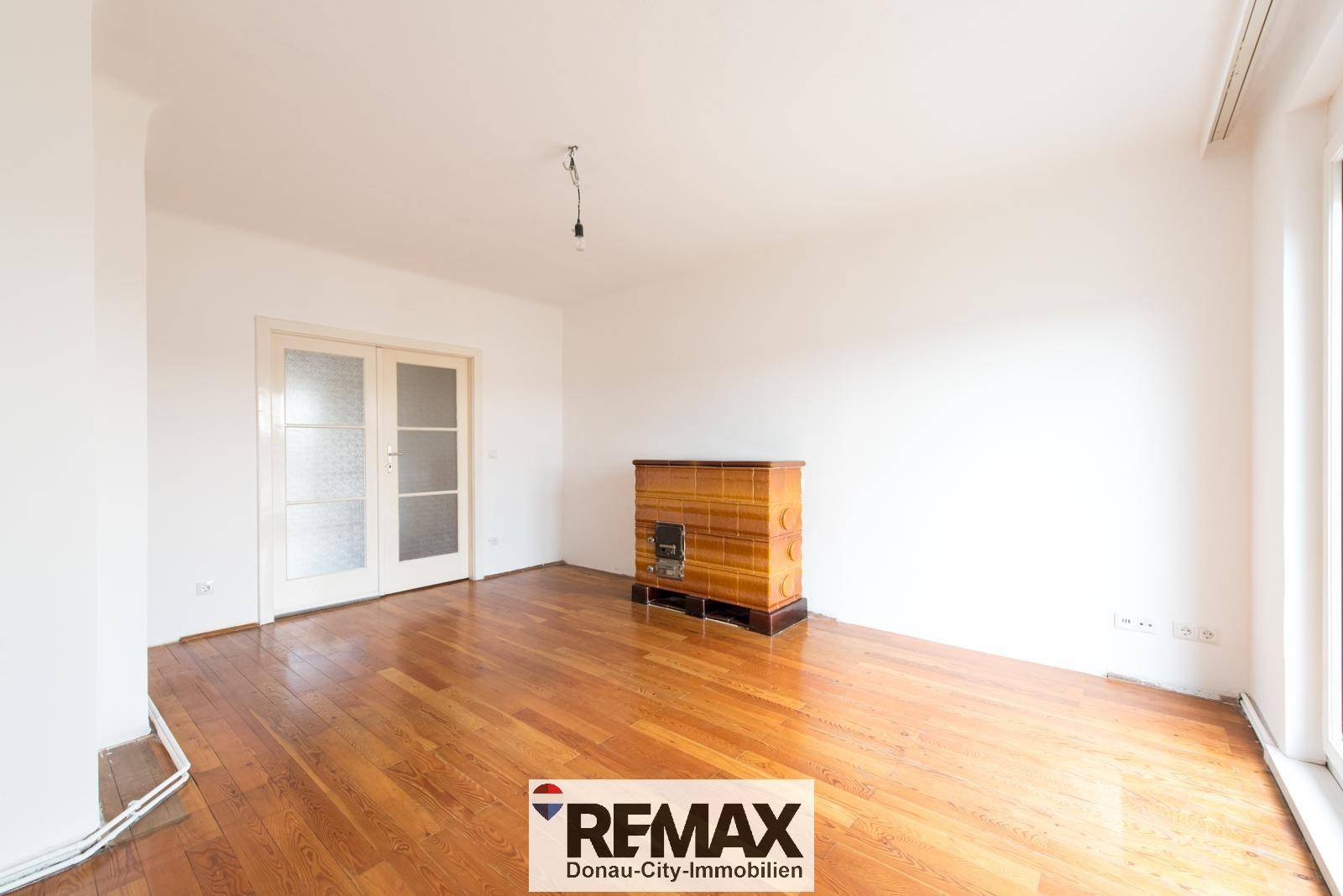Helles Wohnzimmer mit Holzparkettboden, einem Kachelofen und Doppeltüren.