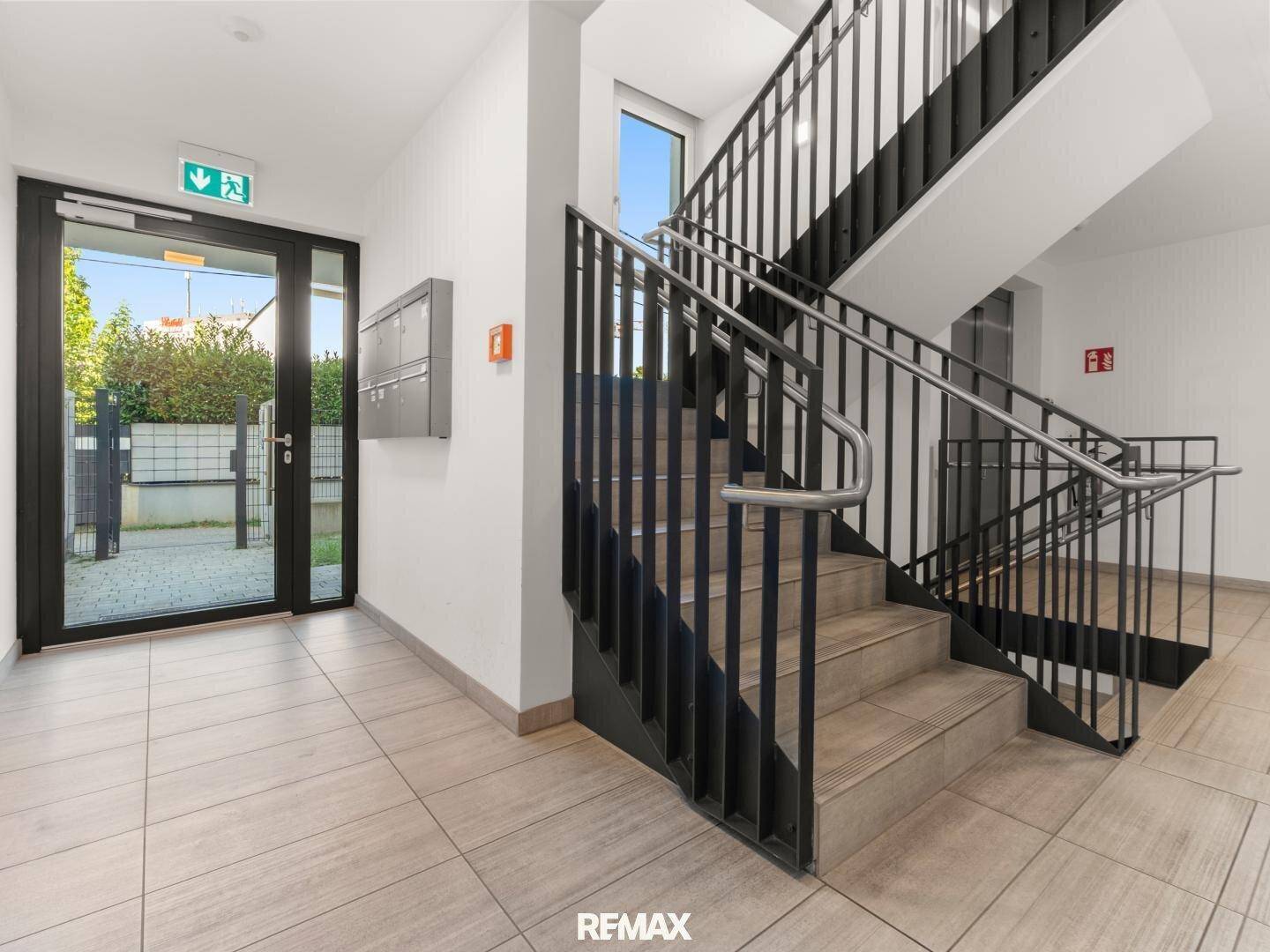 Heller Eingangsbereich mit moderner Treppe und Fliesenboden in einem Mehrfamilienhaus.