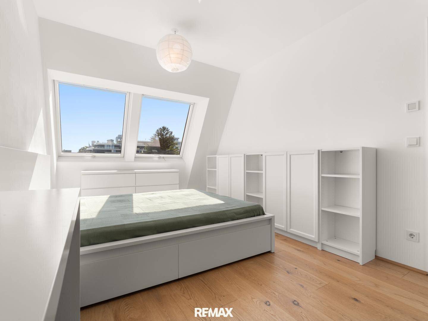 Geräumiges Schlafzimmer mit Holzboden, Dachfenstern und zusätzlichen Regalelementen.