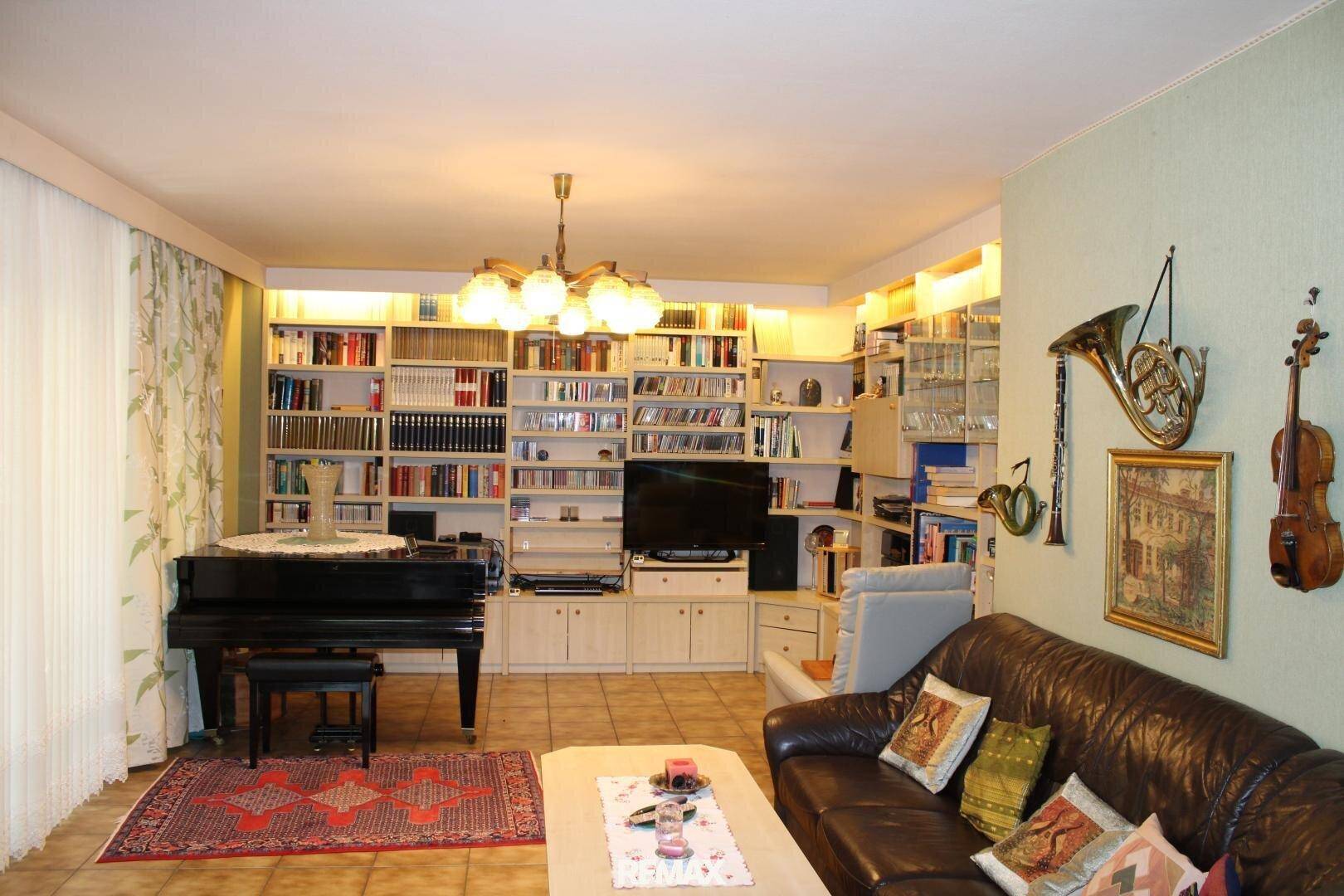 Gemütliches Wohnzimmer mit Ledersofa, umfangreichen Bücherregalen und einem eleganten Flügel.