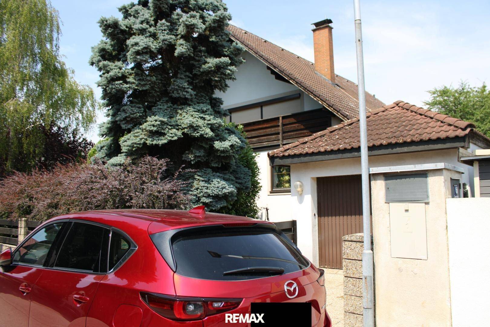Seitenansicht des Hauses mit Garage und einem geparkten roten Auto davor.