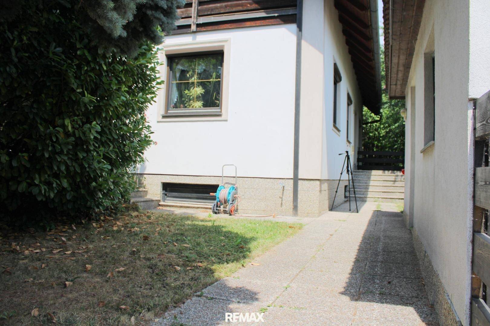 Seitenansicht des Hauses mit einem schmalen Gartenbereich und einem gepflasterten Weg.
