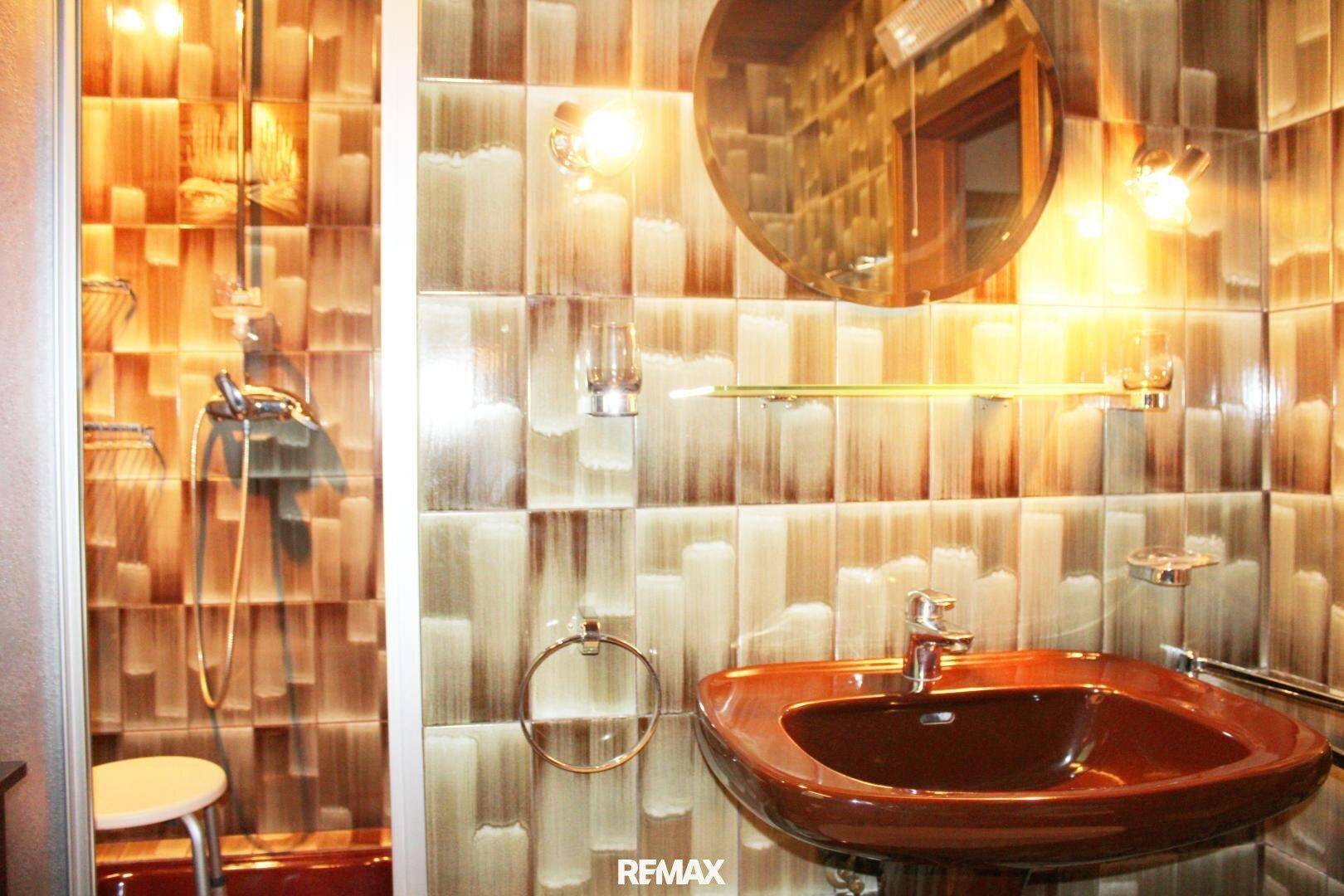 Badezimmer mit braunem Waschbecken, gemusterten Fliesen und einer Duschkabine.