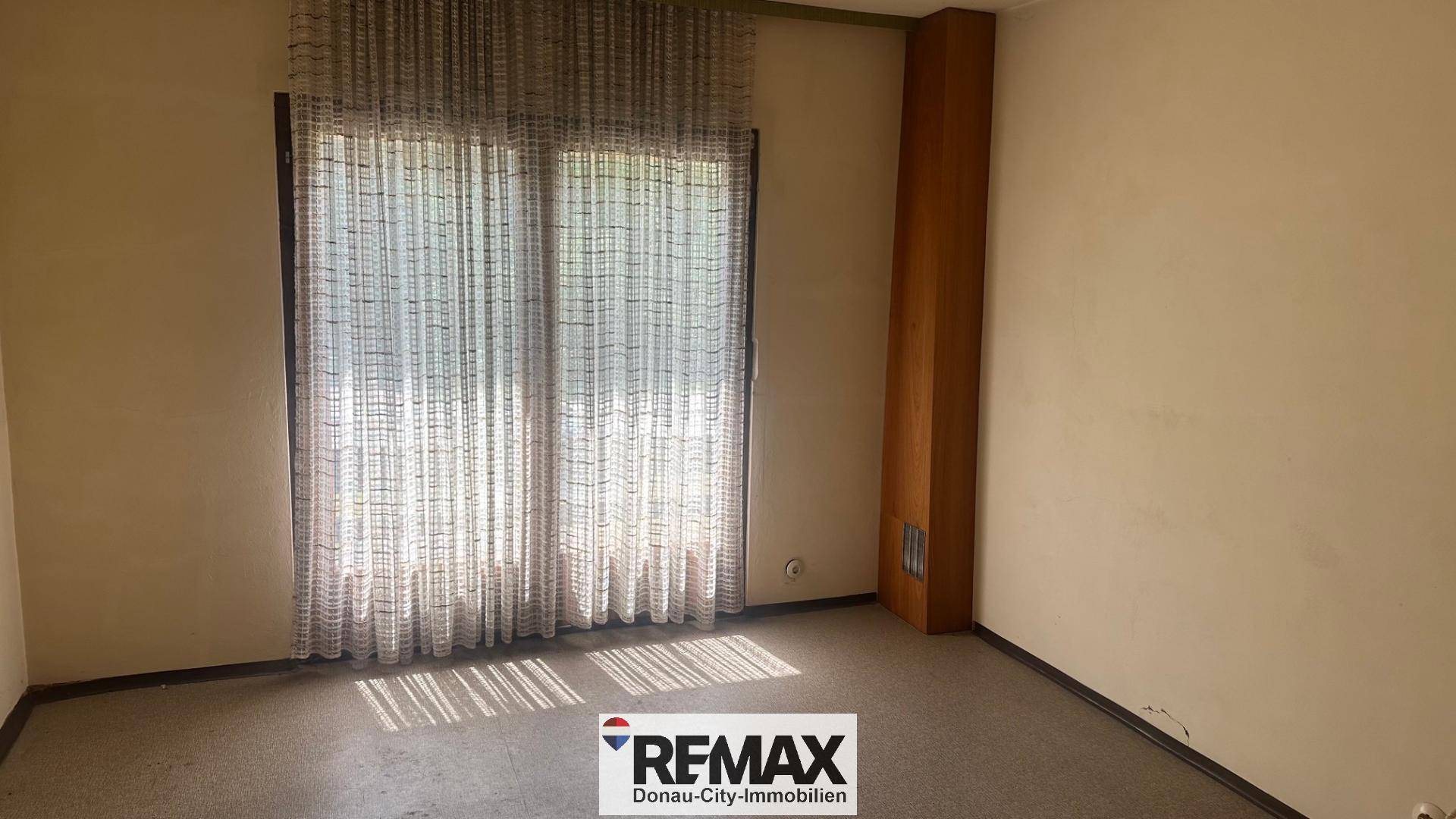 Helles Zimmer mit Fenster und Vorhängen, bereit für eine Renovierung.