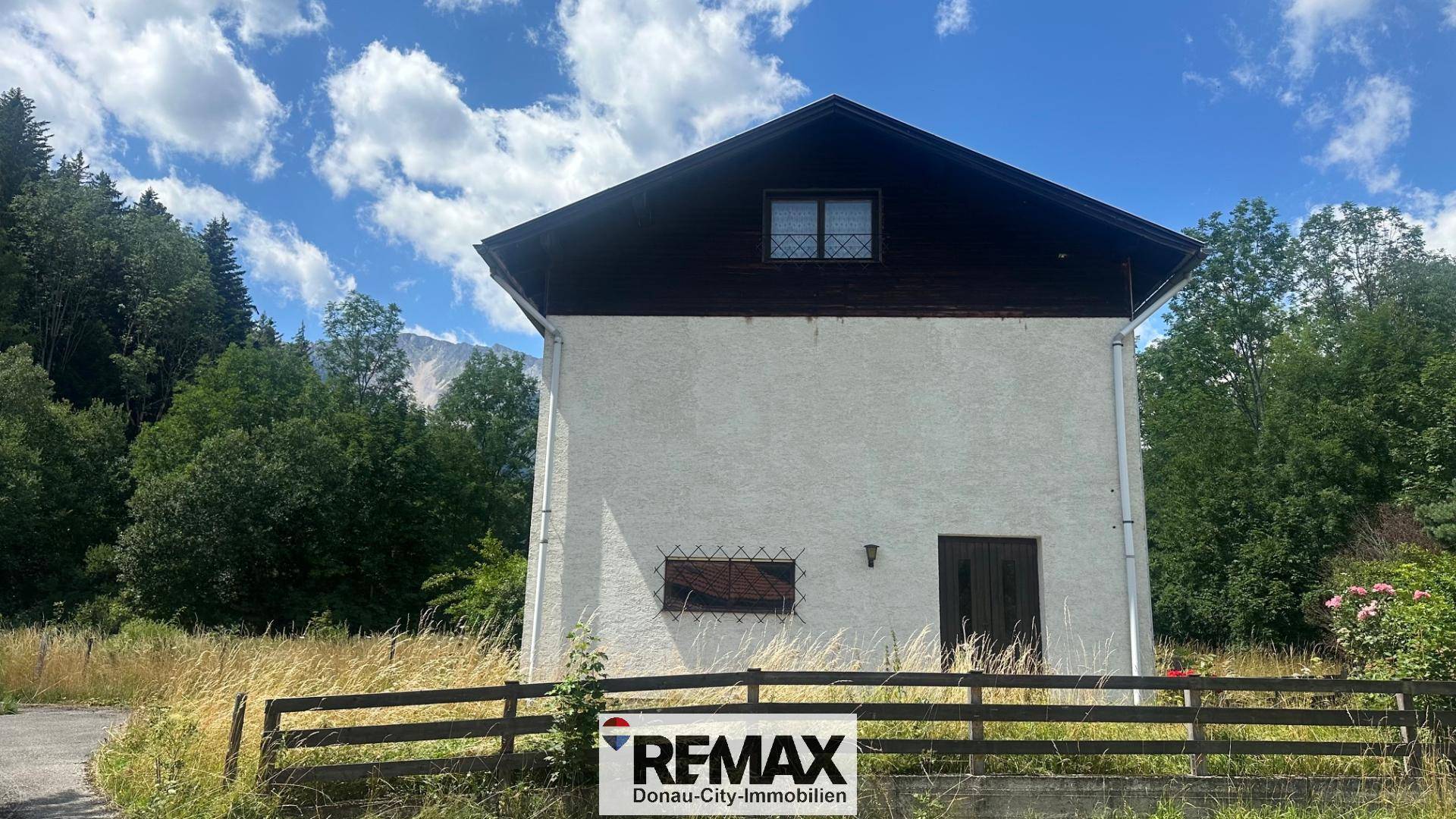 Rückansicht des Hauses mit weißer Fassade und Satteldach, umgeben von Bäumen.