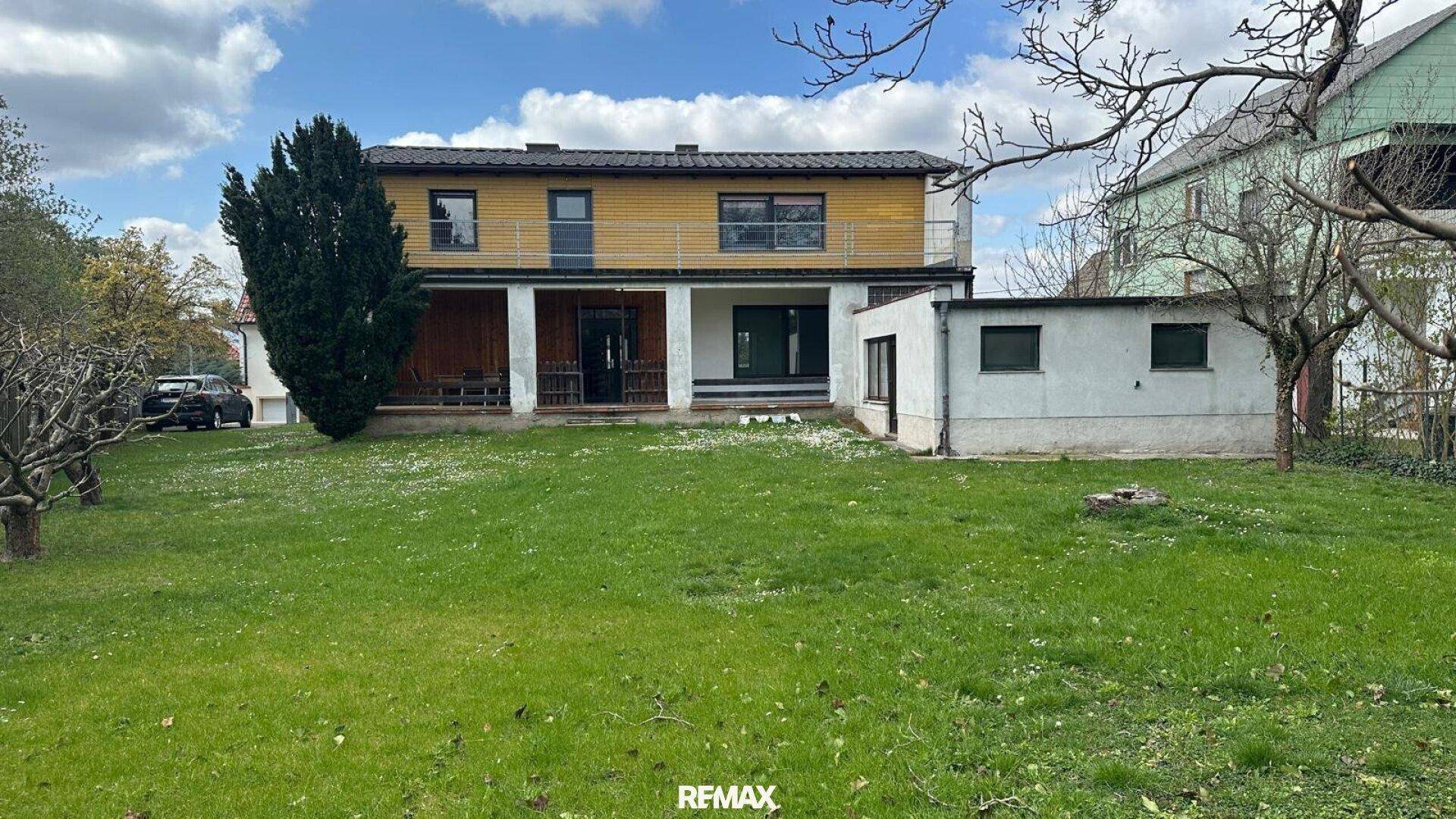 Rückansicht des Hauses mit großem Garten, Rasenfläche und einer überdachten Terrasse im Erdgeschoss.