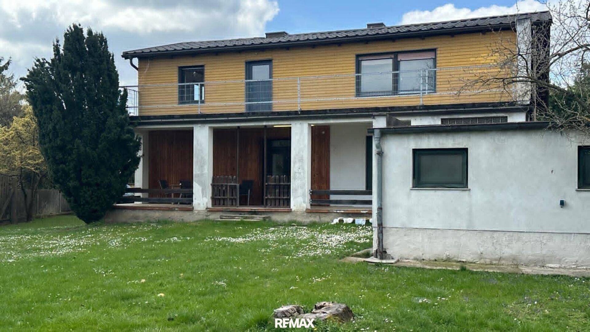 Weitläufiger Gartenbereich hinter dem Haus mit Rasenfläche und Blick auf die überdachte Terrasse.
