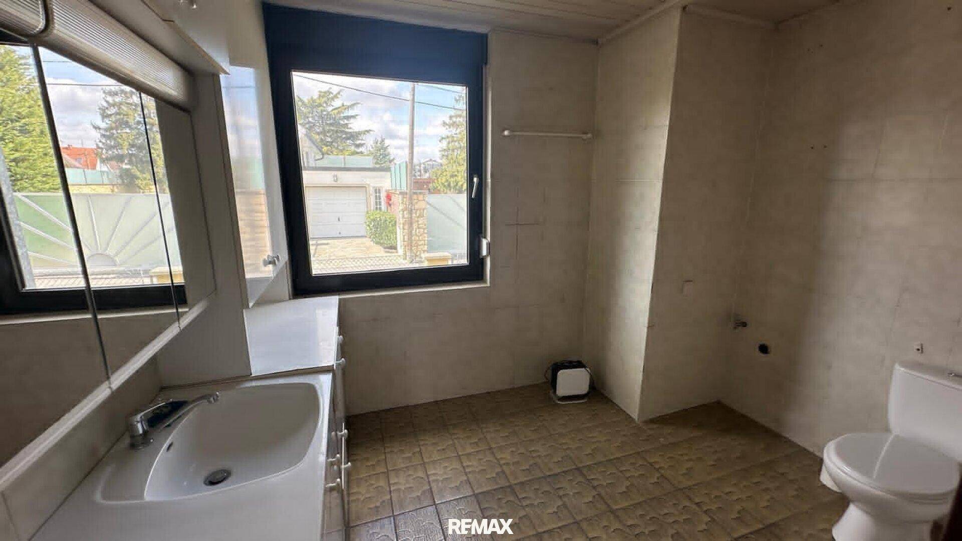 Badezimmer mit Waschbecken, Toilette und Fenster mit Blick auf die Einfahrt.