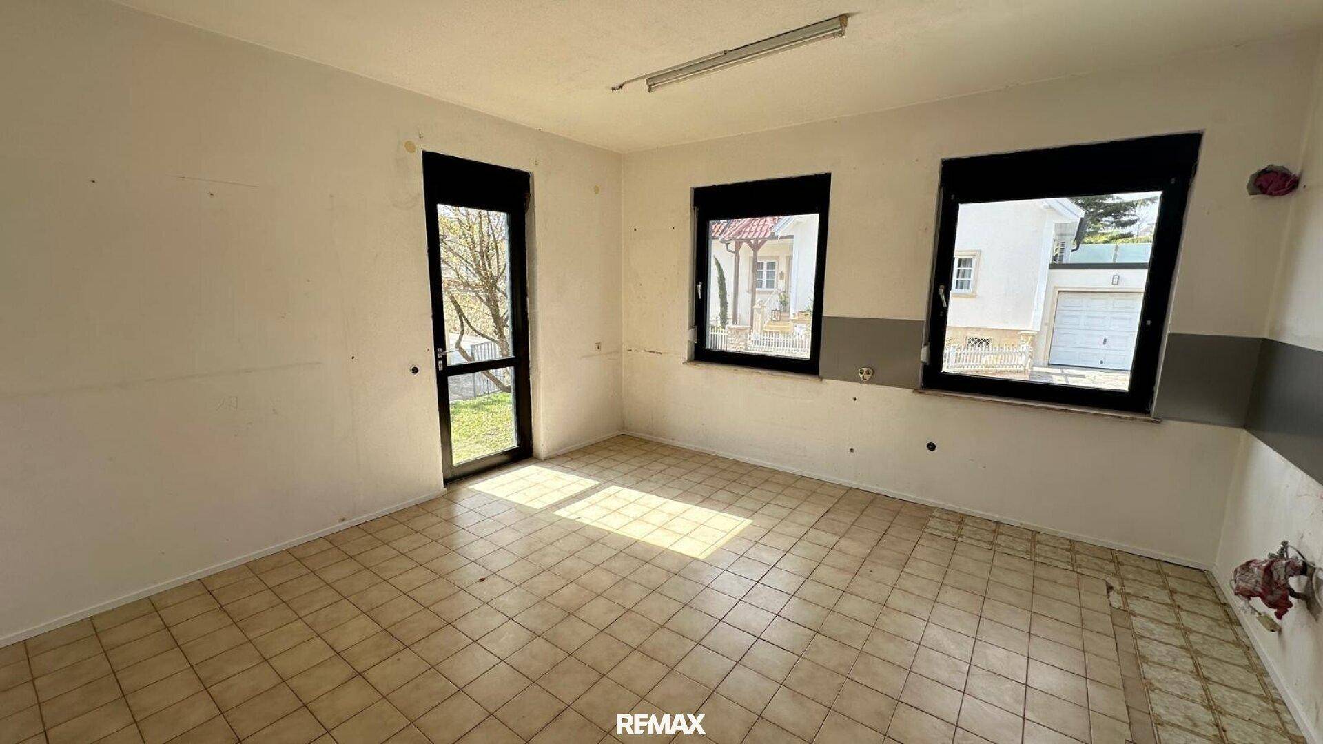 Renovierungsbedürftiger Raum mit Fliesenboden und mehreren Fenstern, die viel Tageslicht hereinlassen.