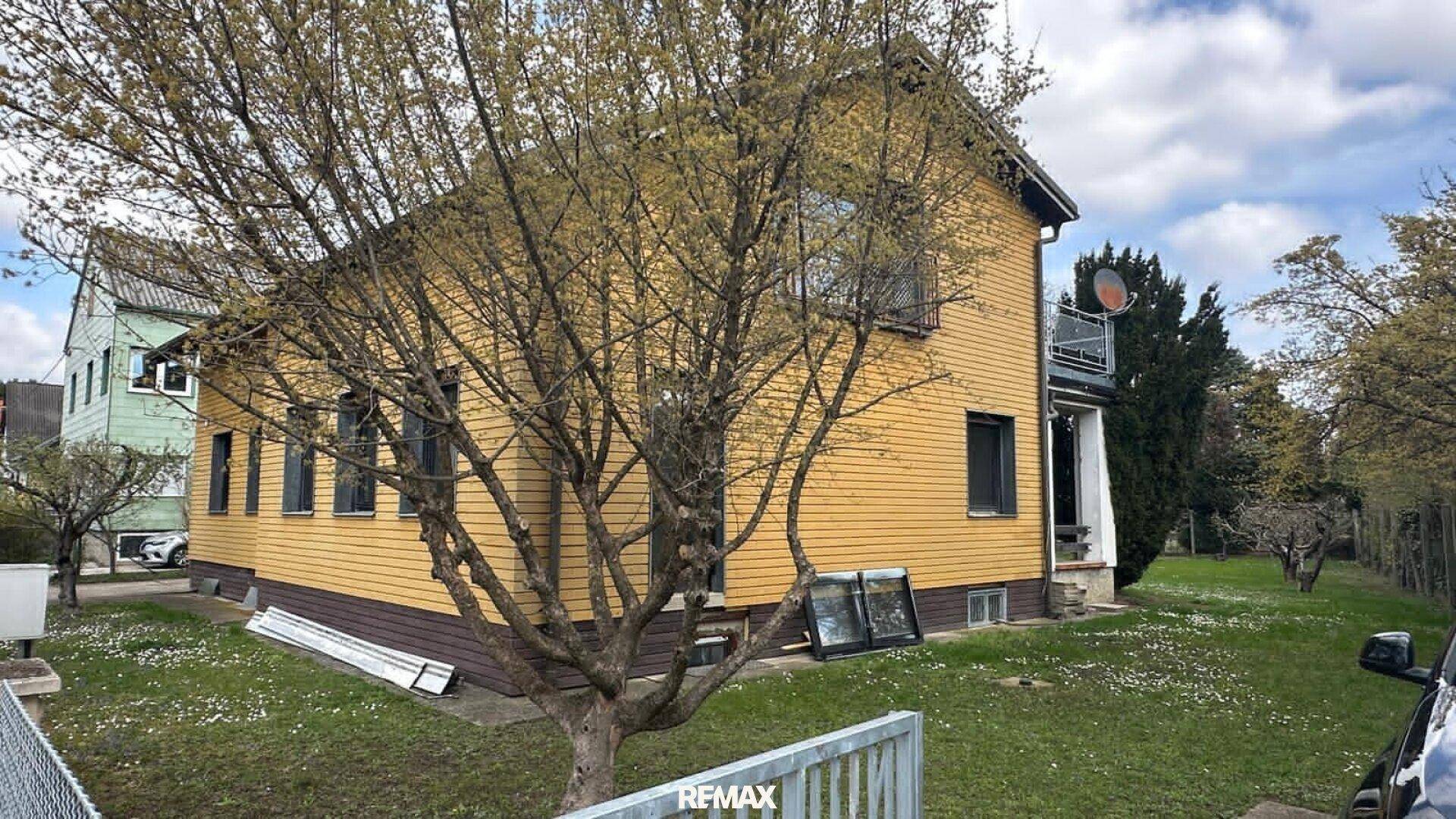 Seitenansicht des Hauses mit großem Gartenbereich und blühenden Bäumen im Frühling.