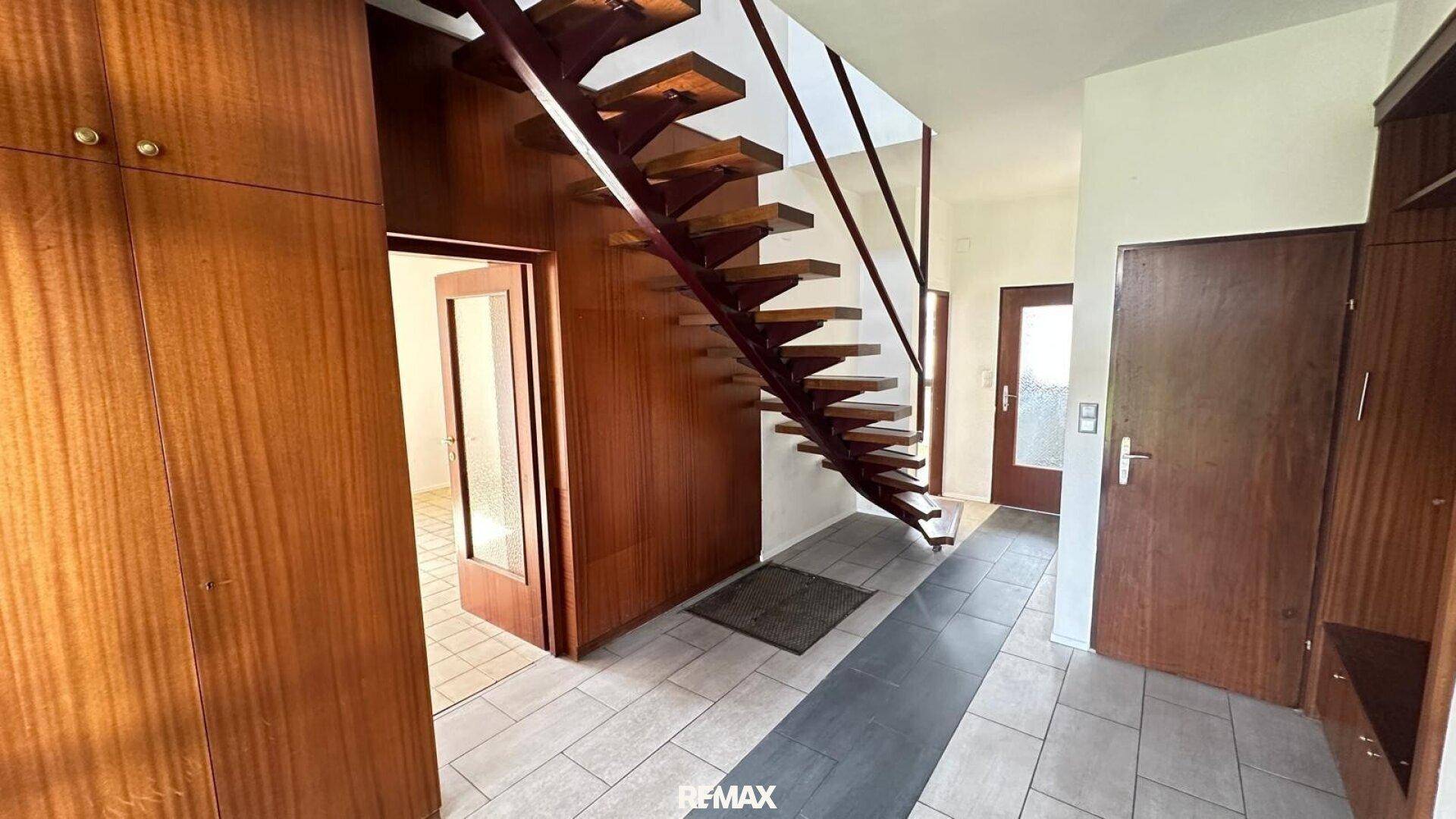 Eingangsbereich mit offener Holztreppe, Einbauschränken und Fliesenboden.