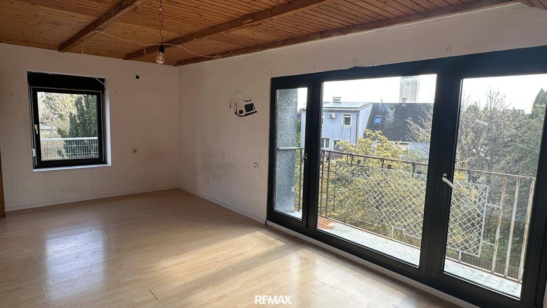 Helles Zimmer mit Holzbalkendecke, Laminatboden und großem Fenster mit Balkonzugang.