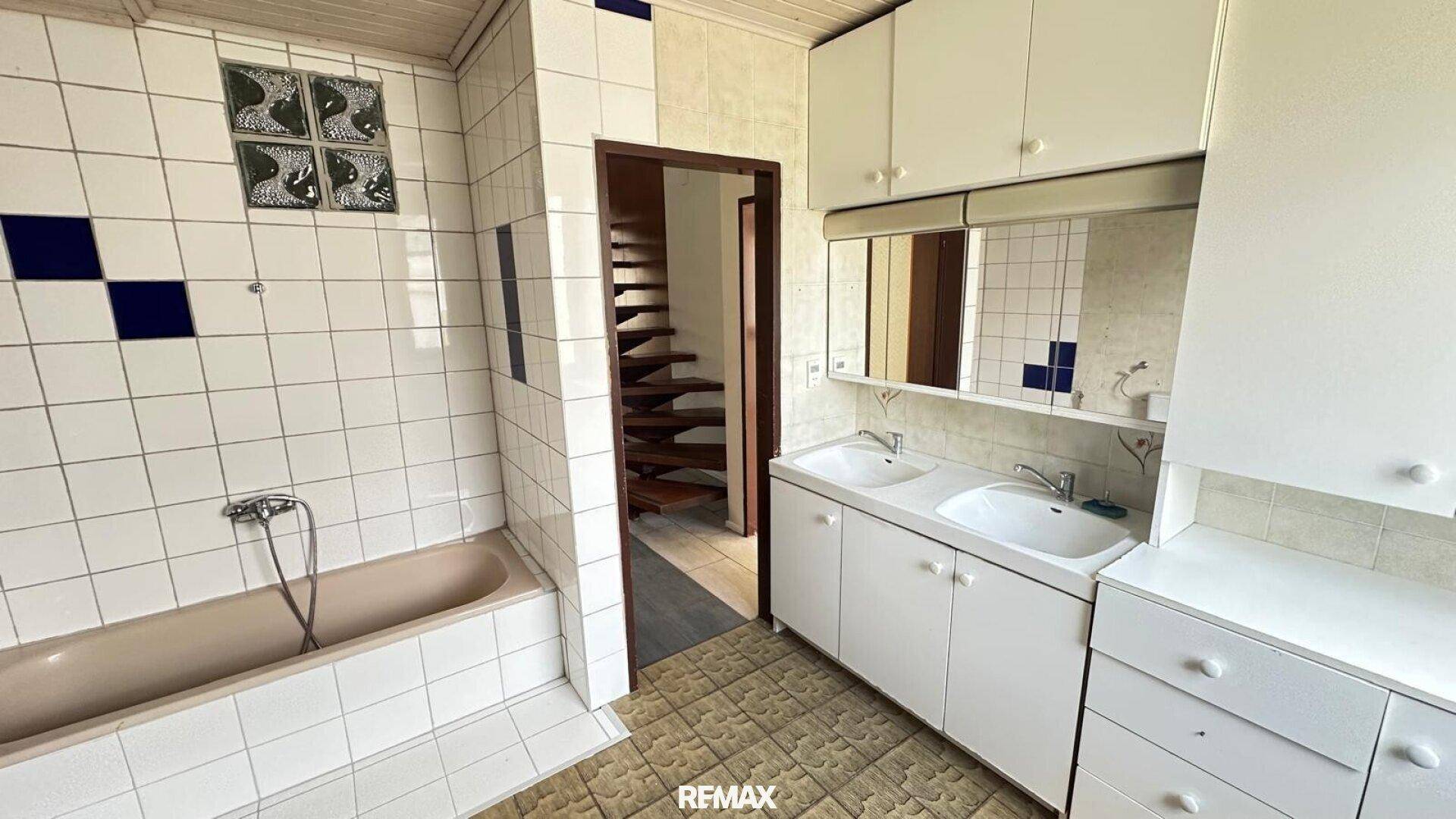 Badezimmer mit Badewanne, Doppelwaschbecken und Fliesen im Stil der 80er Jahre.