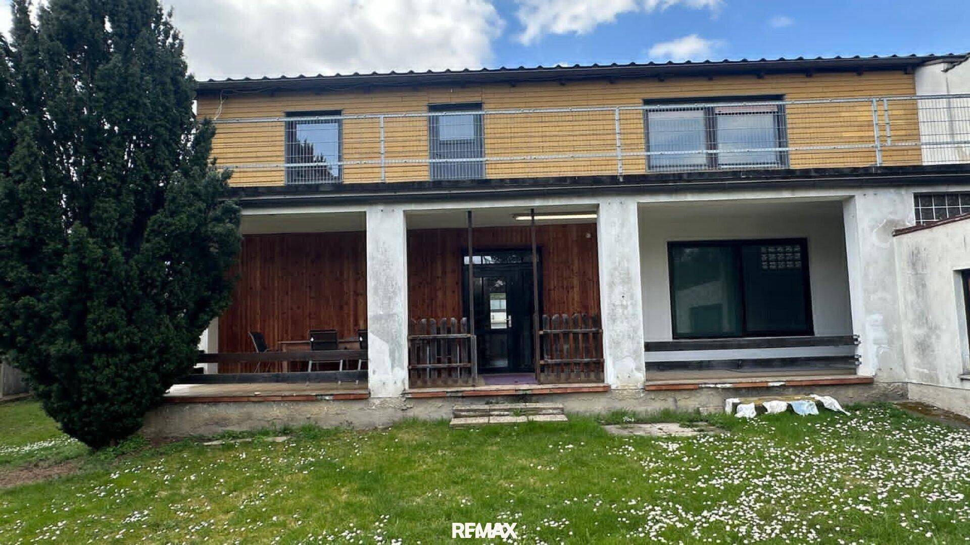 Rückansicht des Hauses mit großem Garten, Rasenfläche und überdachter Terrasse im Erdgeschoss.