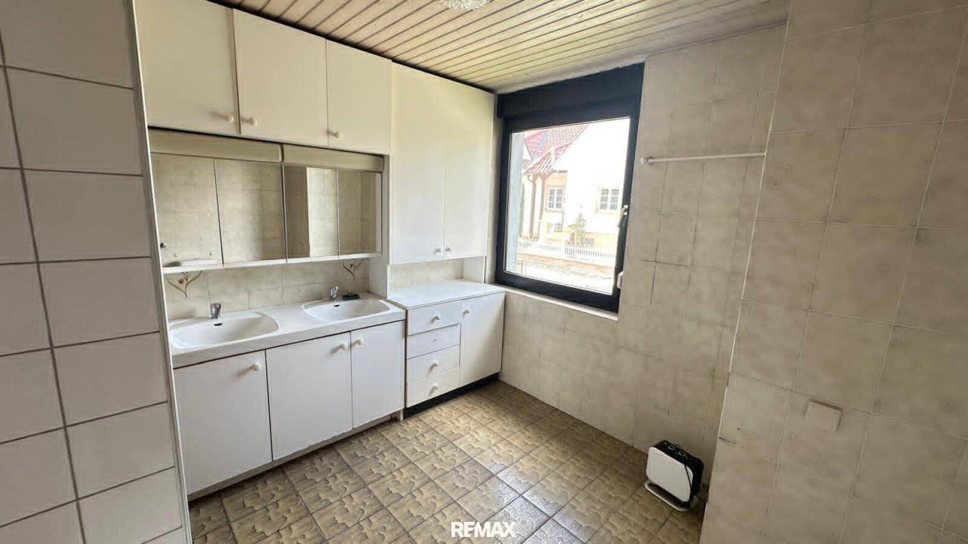 Badezimmer mit Doppelwaschbecken, Spiegelschrank und Fliesen im Stil der 80er Jahre.