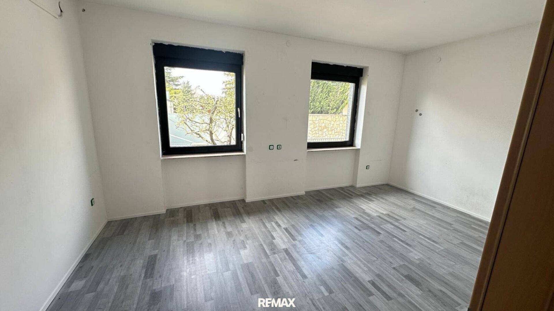 Schlafzimmer mit modernem Laminatboden und zwei Fenstern für viel Tageslicht.