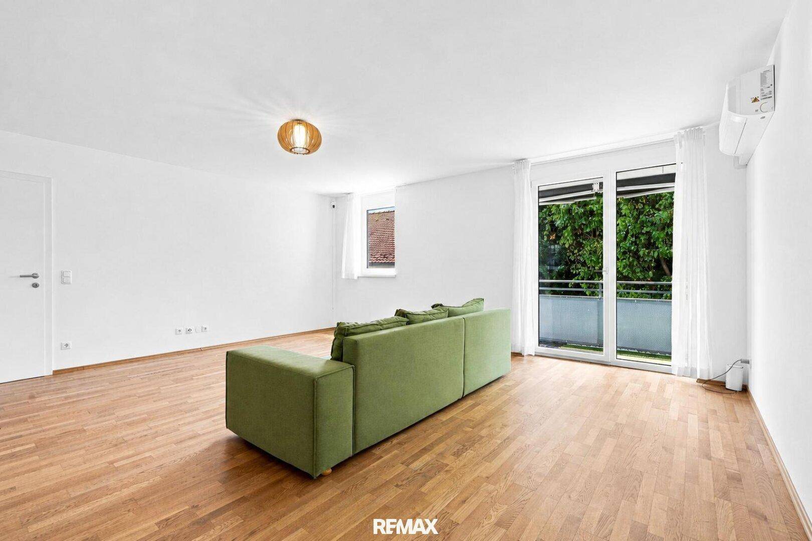 Großzügiges Wohnzimmer mit Holzboden, Klimaanlage und Zugang zum sonnigen Balkon.