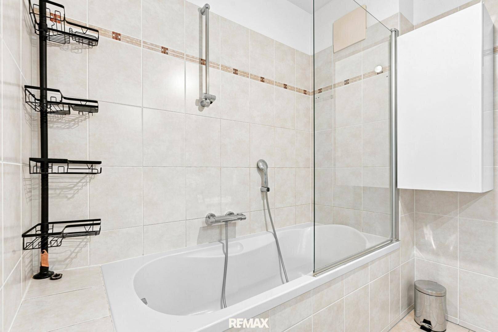 Helles Badezimmer mit Badewanne und Duschabtrennung, komplett gefliest.