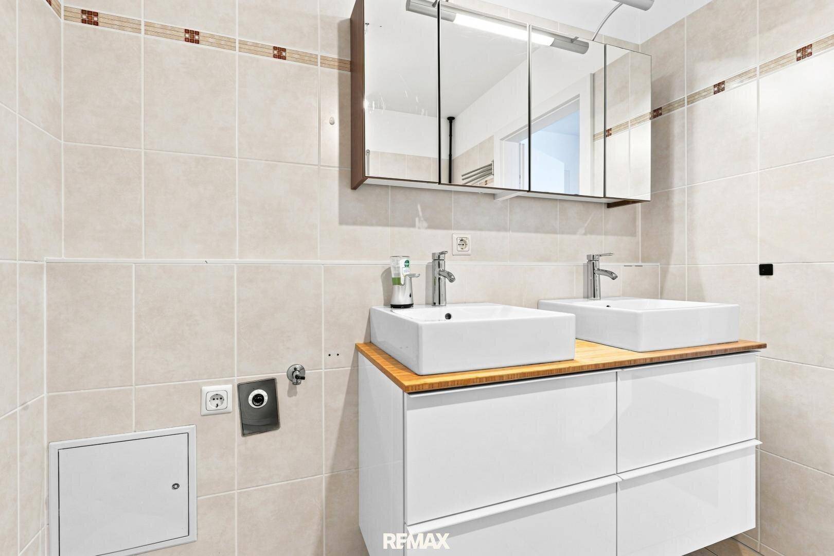 Modernes Badezimmer mit Doppelwaschbecken, Spiegelschrank und hellen Fliesen.