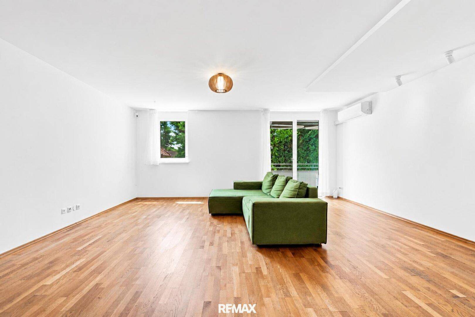 Helles Wohnzimmer mit bequemer grüner Couch, Holzboden und großen Fenstern für viel Tageslicht.