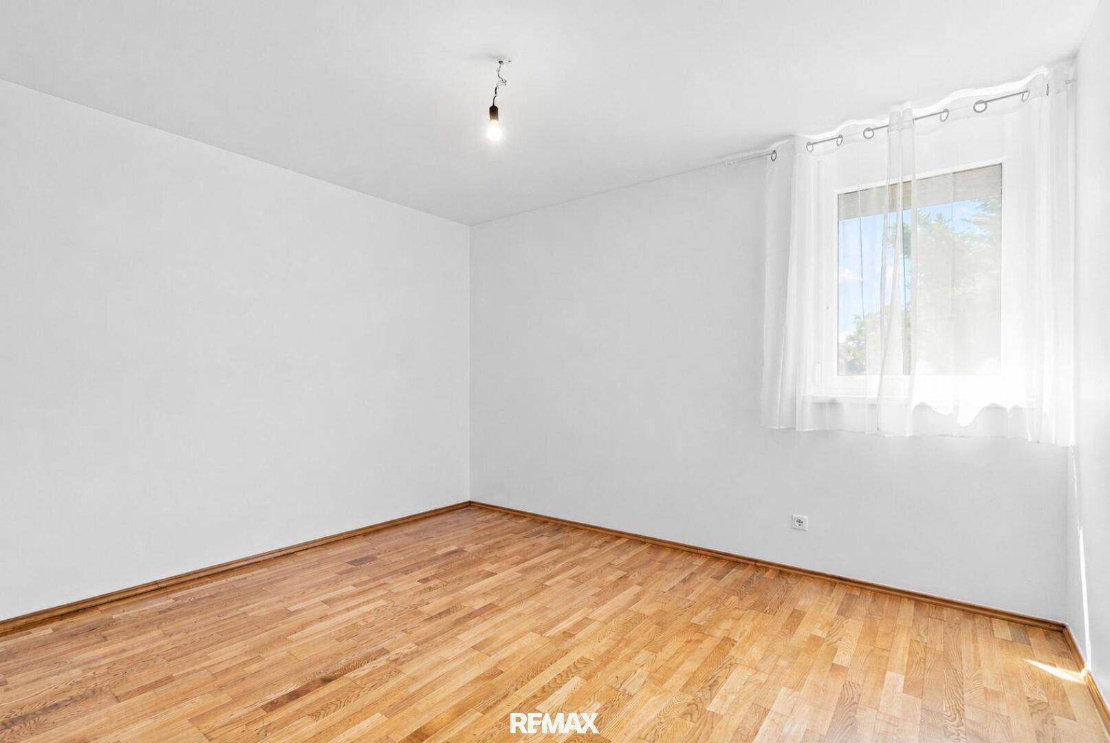 Freundliches Zimmer mit Holzboden und großem Fenster, ideal für ein Schlafzimmer.