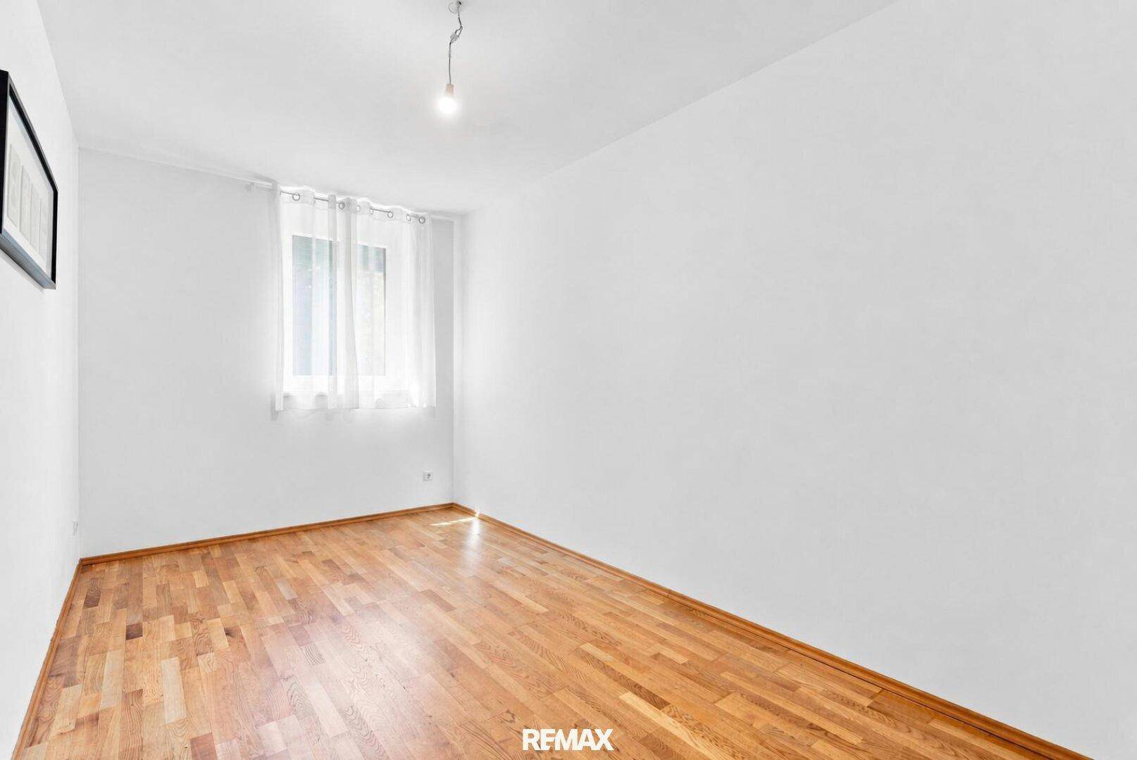 Freundliches Zimmer mit Holzboden und großem Fenster, ideal als Kinder- oder Gästezimmer.