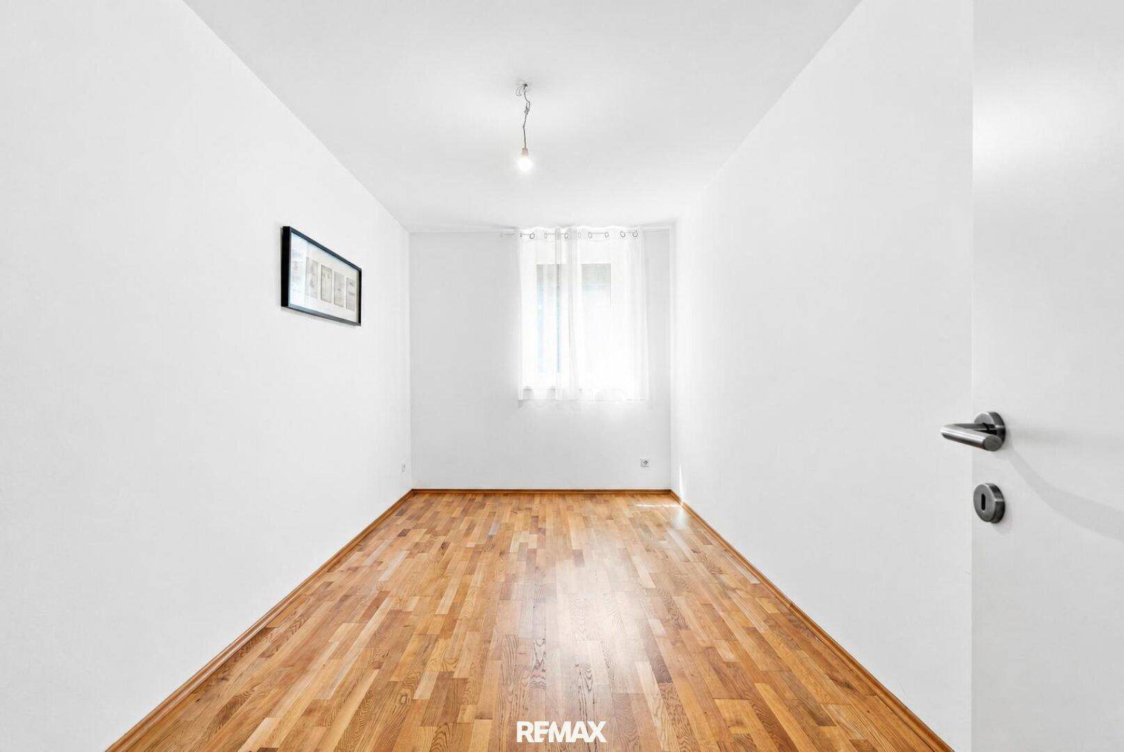 Helles, leeres Zimmer mit Holzboden und Fenster, vielseitig nutzbar als Schlaf- oder Arbeitszimmer.