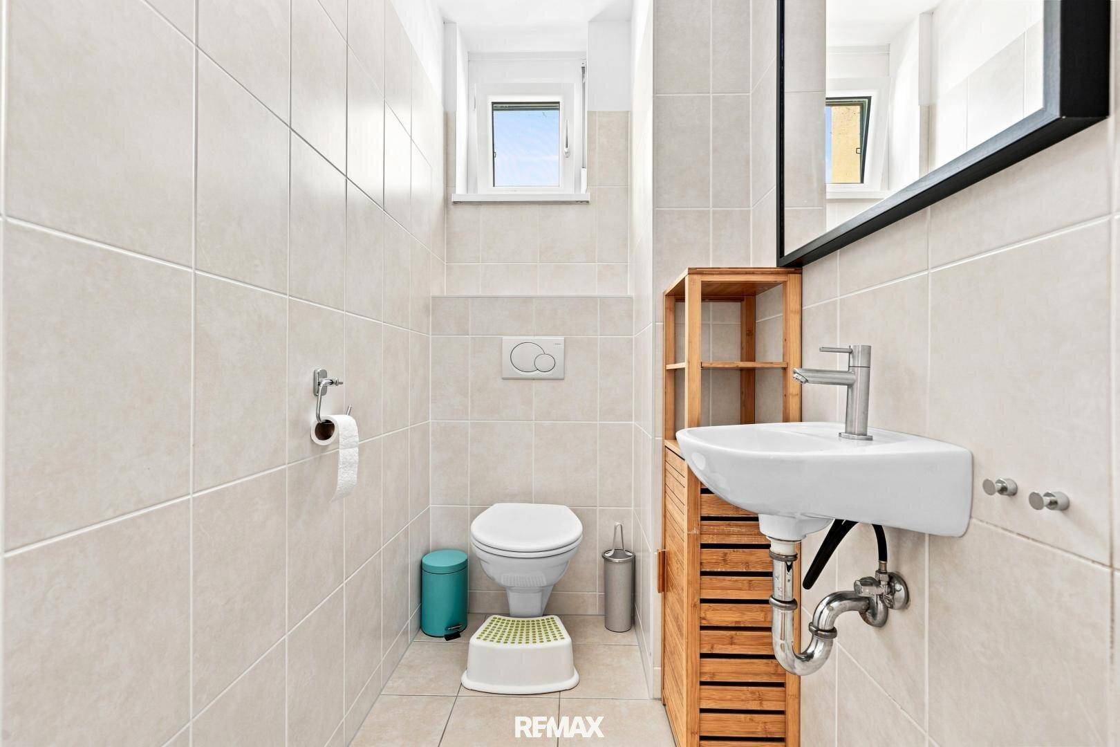 Modernes Gäste-WC mit Wand-WC, Waschbecken und Fenster für natürliche Belüftung.